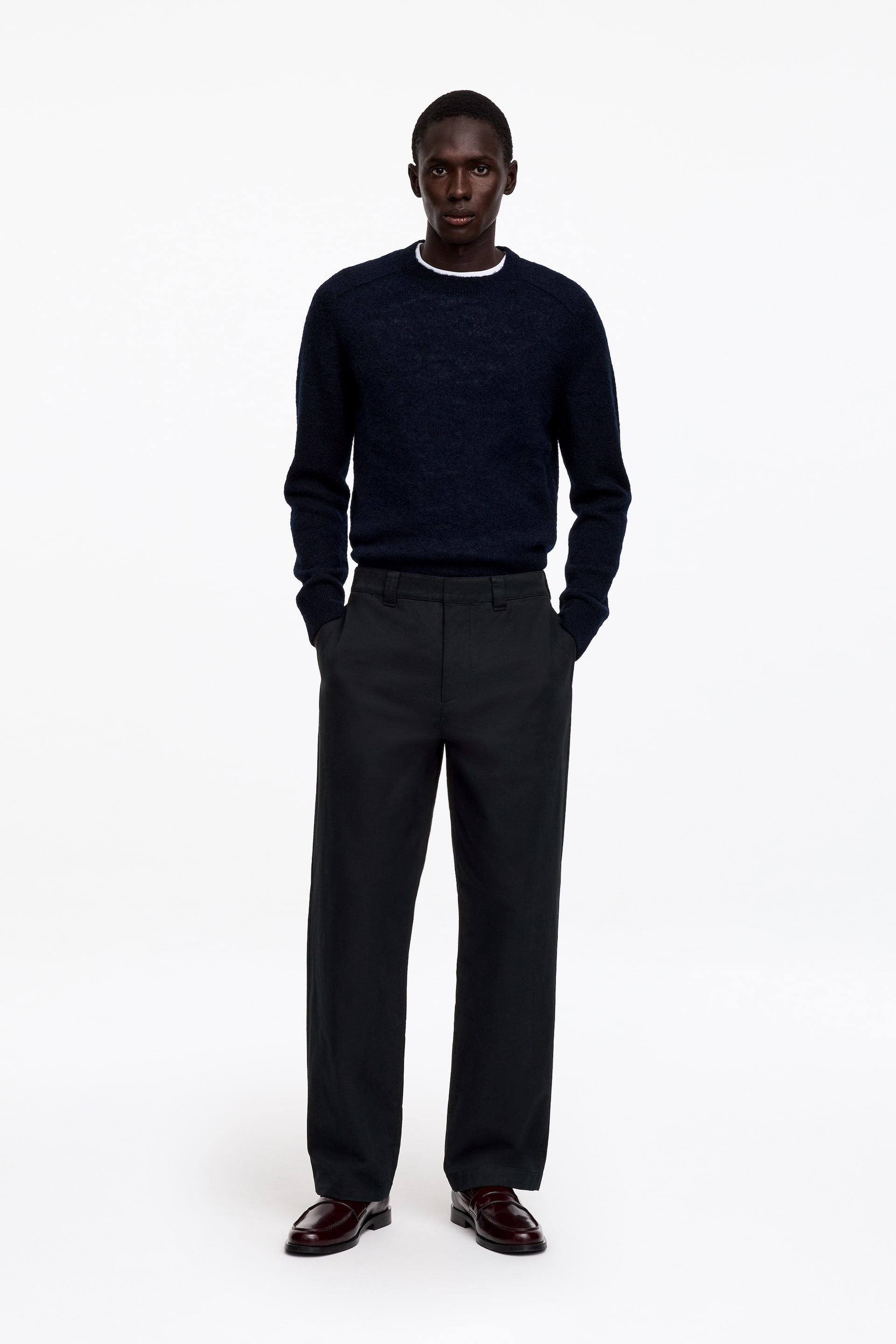 Ver imagen más grande: Estos chinos de trabajo de ajuste ancho, en color gris oscuro, los lleva la modelo, que está de pie con las manos colocadas en los bolsillos delanteros inclinados. El pantalón presenta trabillas anchas para el cinturón y un corte recto de pernera, y aquí se combina con un jersey azul marino metido por dentro y mocasines de cuero oscuro.