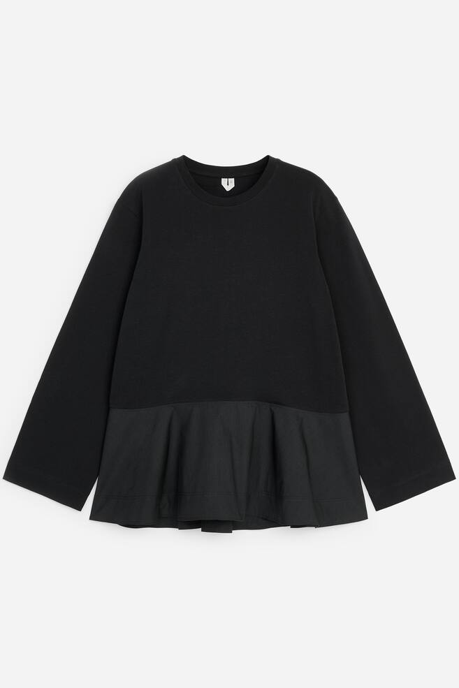 Uma camisola preta de manga comprida, vista de frente, apresenta um tronco em jersey mate com decote redondo clÃ¡ssico e mangas largas e direitas. O design transita para uma bainha peplum franzida e evasÃ©, em tecido entranÃ§ado contrastante, ligeiramente texturado. - 1