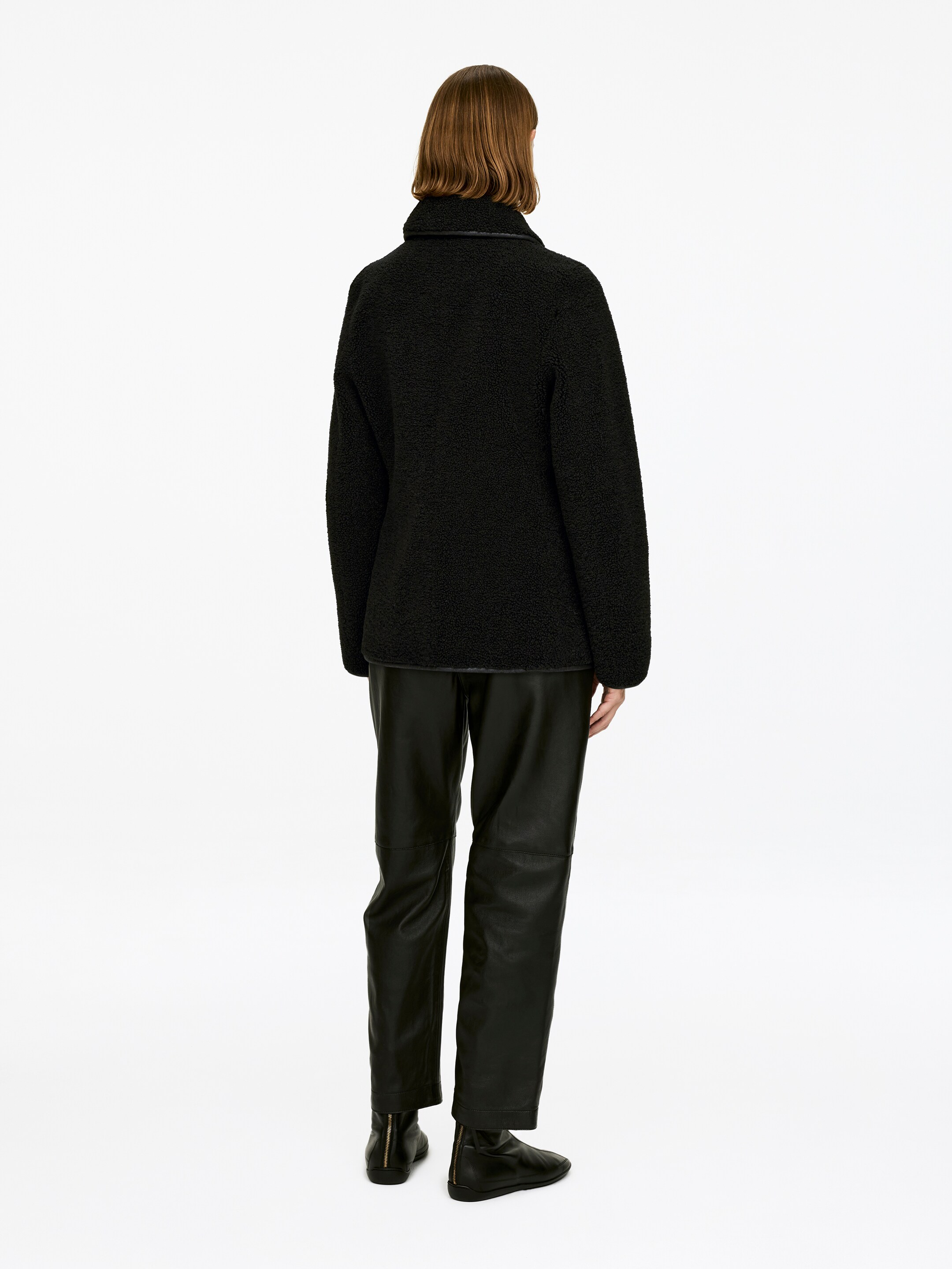 View larger image: A black pile jacket featuring a classic collar is being worn by the model. The model is styling the jacket with black trousers and boots.