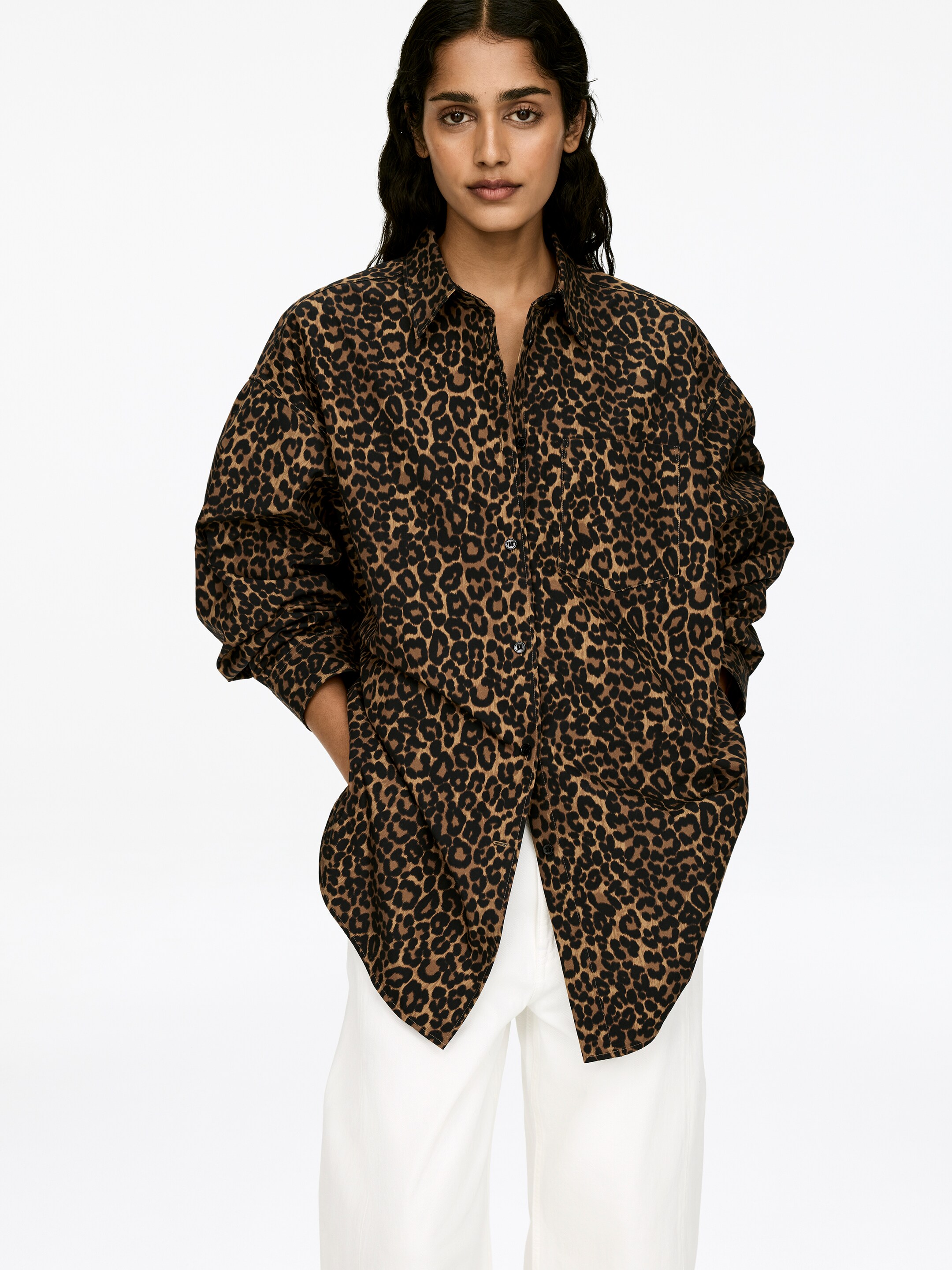 Größeres Bild ansehen: Ein übergroßes Leopardenmusterhemd mit Fledermausärmeln und einer einzigen Brusttasche wird von dem Model getragen. Das Hemd ist mit geöffneten oberen Knöpfen gestylt.
