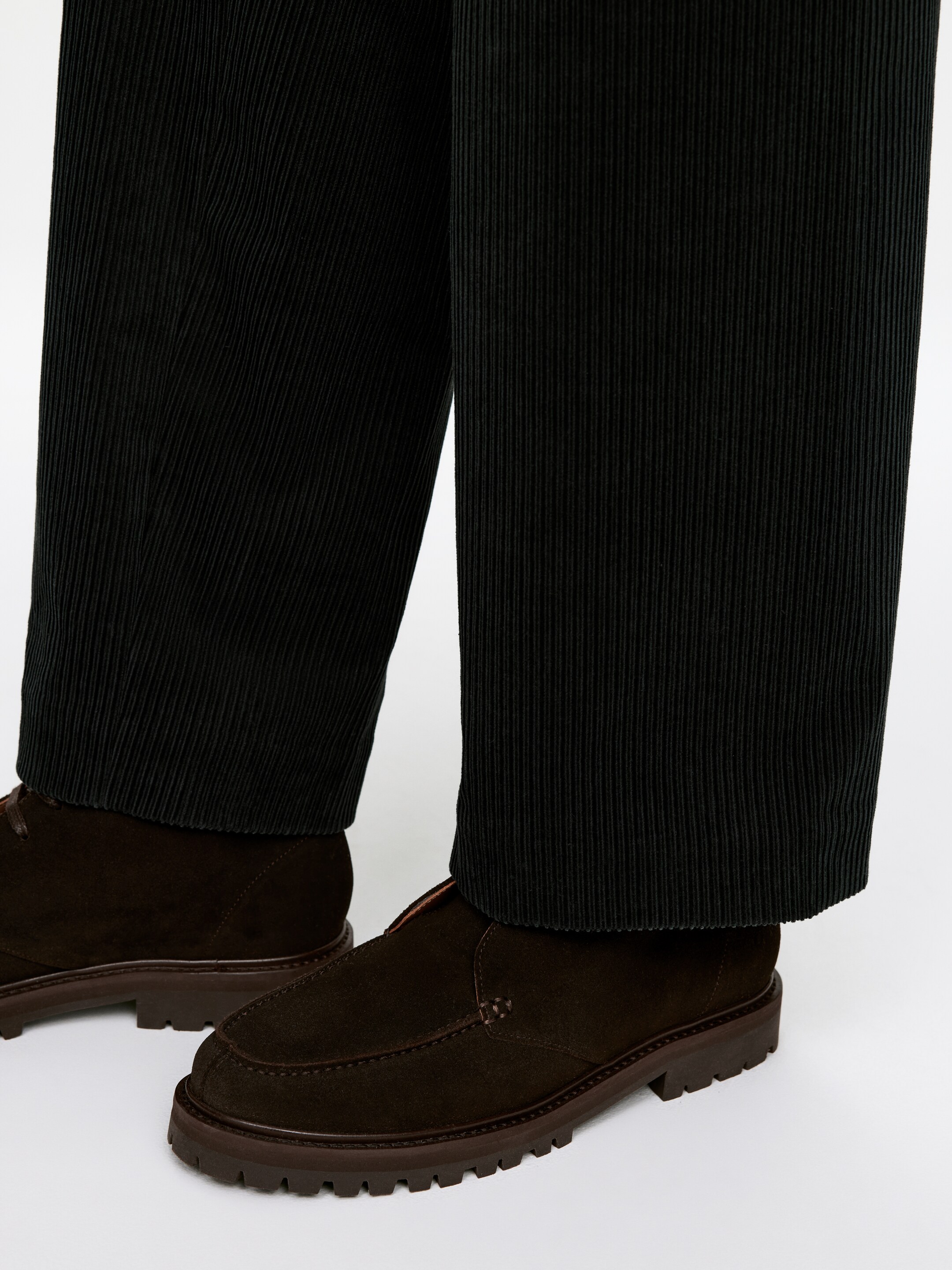 Grotere afbeelding bekijken: Donkergroene wijde broek met een plissétextuur wordt gedragen. Ze vallen over een paar donkerbruine suède moc-toe schoenen, die dikke lugzolen hebben en iets schuin staan, waardoor hun zijprofiel zichtbaar is.