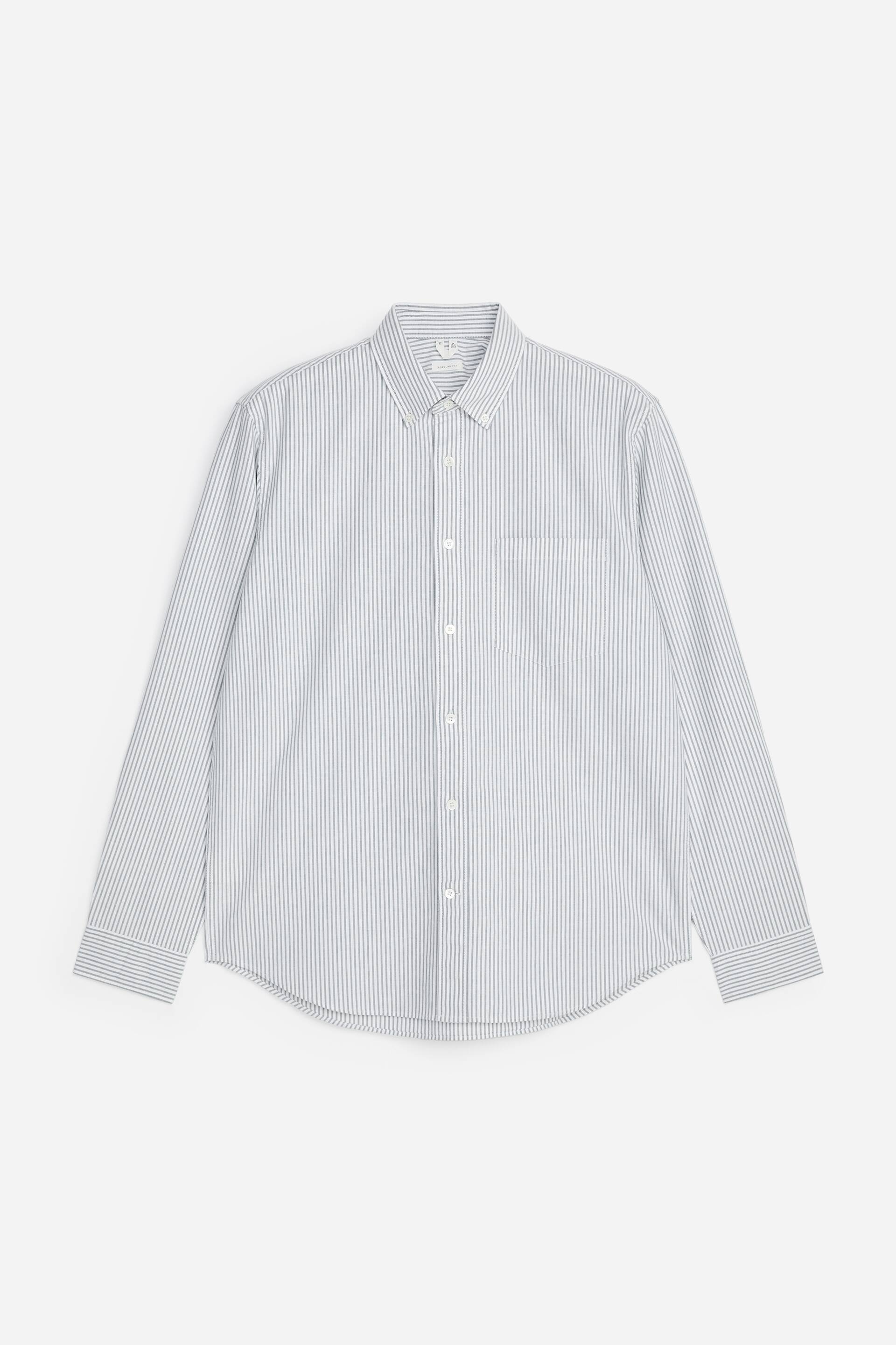 Größeres Bild anzeigen: Ein Oxford-Hemd präsentiert sich in der Vorderansicht, mit dünnen dunklen vertikalen Streifen auf weißem Hintergrund. Es ist mit einem Button-Down-Kragen, einer durchgehenden Knopfleiste mit weißen Knöpfen, einer einzelnen Brusttasche und langen Ärmeln mit geknöpften Manschetten gestaltet.