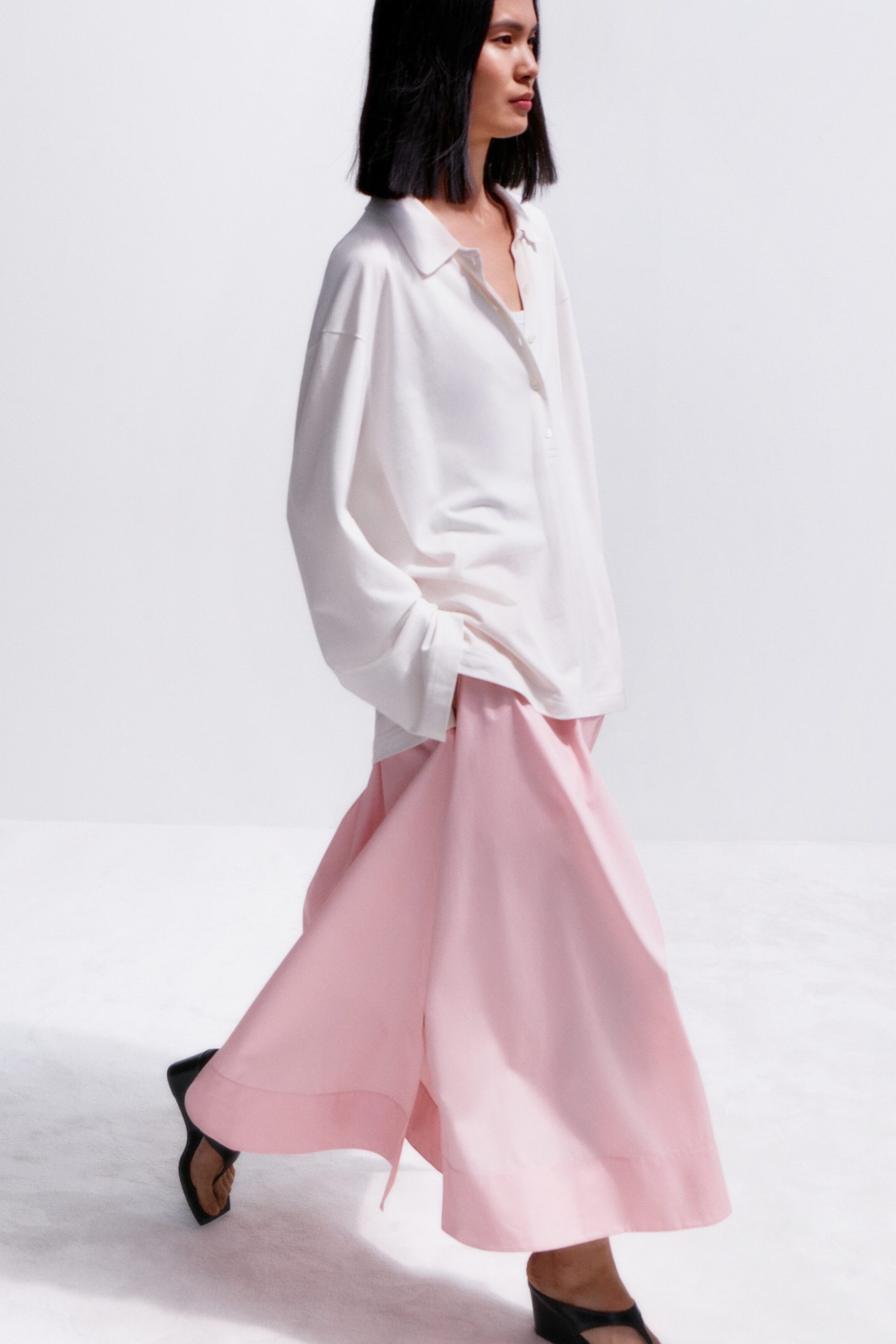 Преглед на по-голямо изображение: Бяла риза с дълги ръкави и класическа яка, с три копчета на предницата, с лежерна кройка, която се спуска свободно. Розови панталони с широки крачоли, които се движат леко, показвайки своята пълна дължина и обемна кройка.