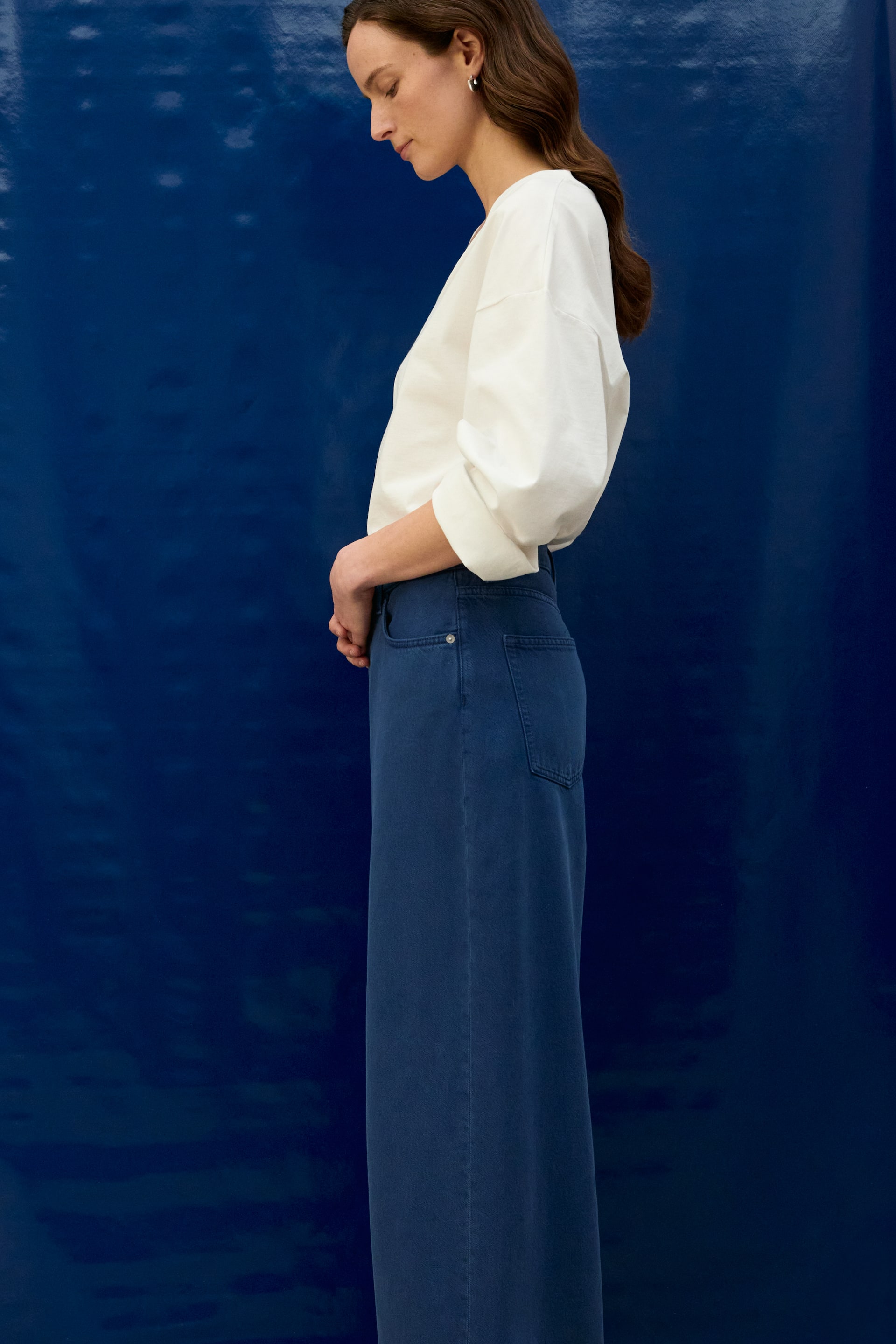 Agrandir l'image: Le pantalon bleu à jambes larges est présenté sous un angle latéral-arrière, avec une taille haute où un haut blanc est rentré. Une poche arrière plaquée visible est située sur le côté droit.