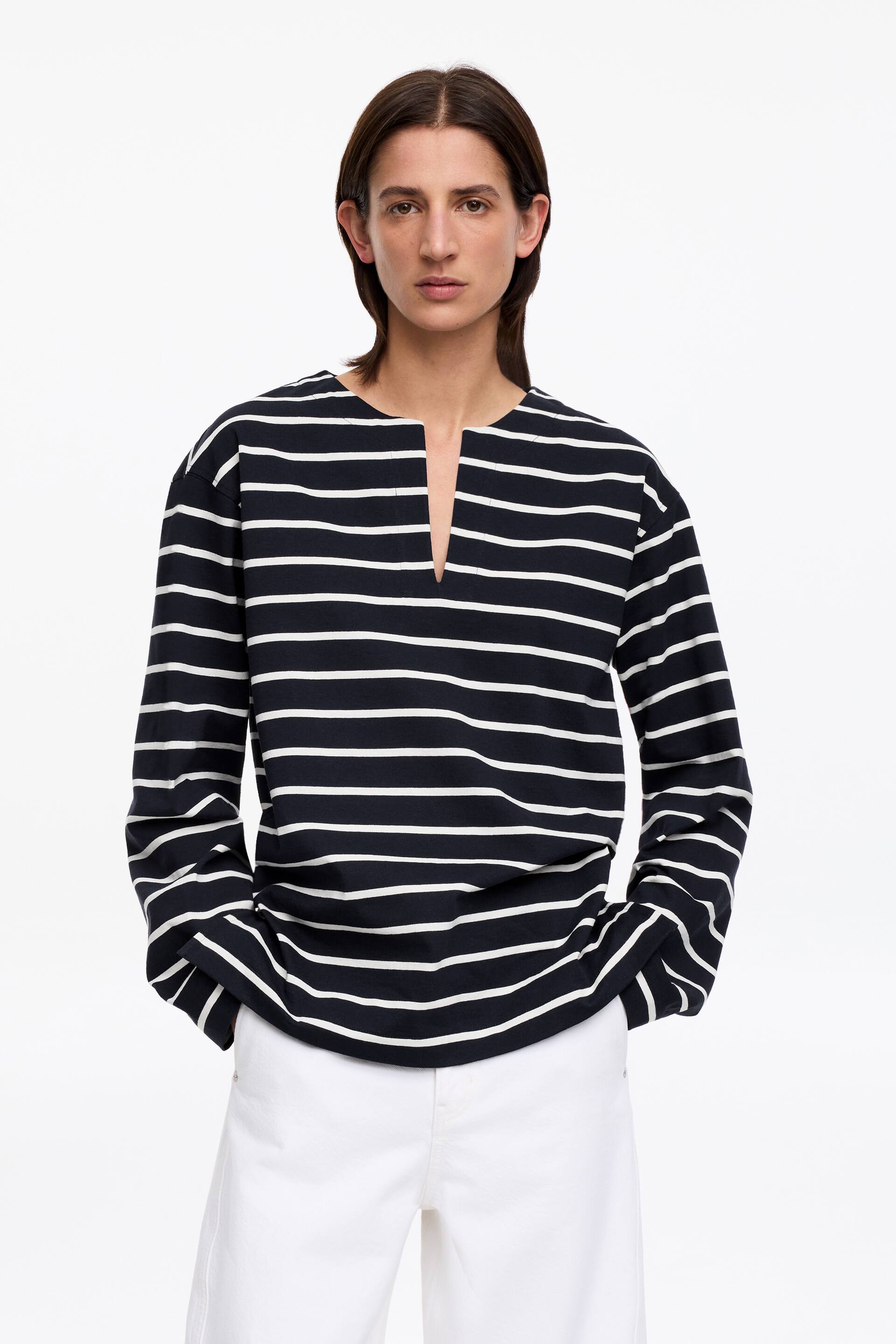 Größeres Bild anzeigen: Ein langärmliges Oberteil mit navyblauen und weißen horizontalen Streifen und einem V-förmigen Halsausschnitt wird vom Model getragen. Das Model steht mit den Händen in den Taschen einer weißen Hose, was den Fall des unteren Saums des Oberteils beeinflusst.