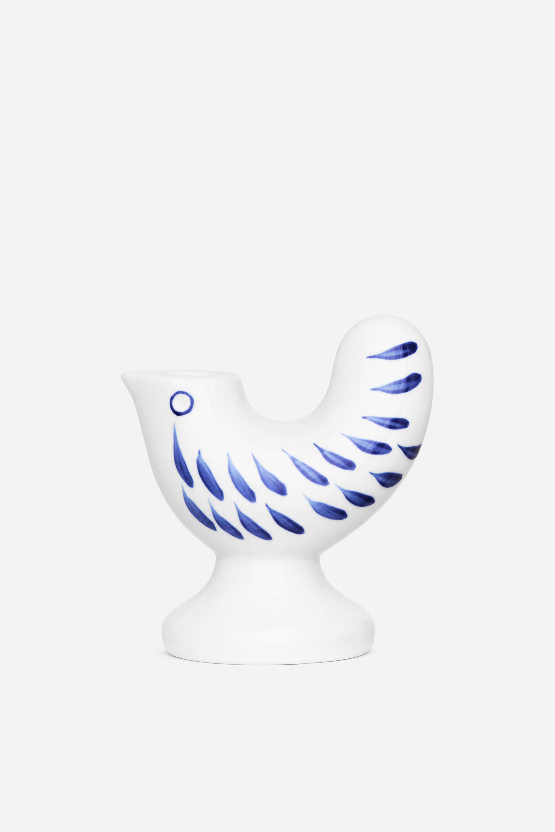 View larger image: A white ceramic bird-shaped vessel is facing FRONT, its body and tail adorned with blue teardrop patterns. A small spout and a blue circular detail are visible on its head, and it rests on a flared pedestal base.