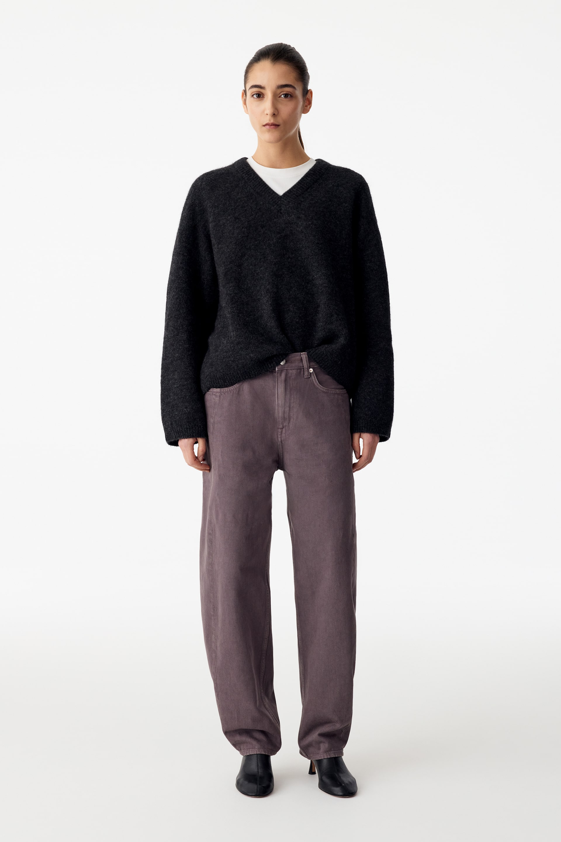 Agrandir l'image: Ce jean en denim violet poudré à coupe décontractée est porté par le mannequin, avec une taille mi-haute et des jambes légèrement sculptées. Le jean est associé à un pull en maille noir à col V porté sur un t-shirt blanc, ainsi qu’à des bottes en cuir noir.