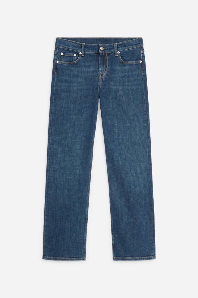 These blue jeans are photographed from the front, featuring a low-rise waist, slim fit, and straight legs. The medium-wash denim showcases classic five-pocket styling, contrast stitching, and silver-tone metal rivets. - 1