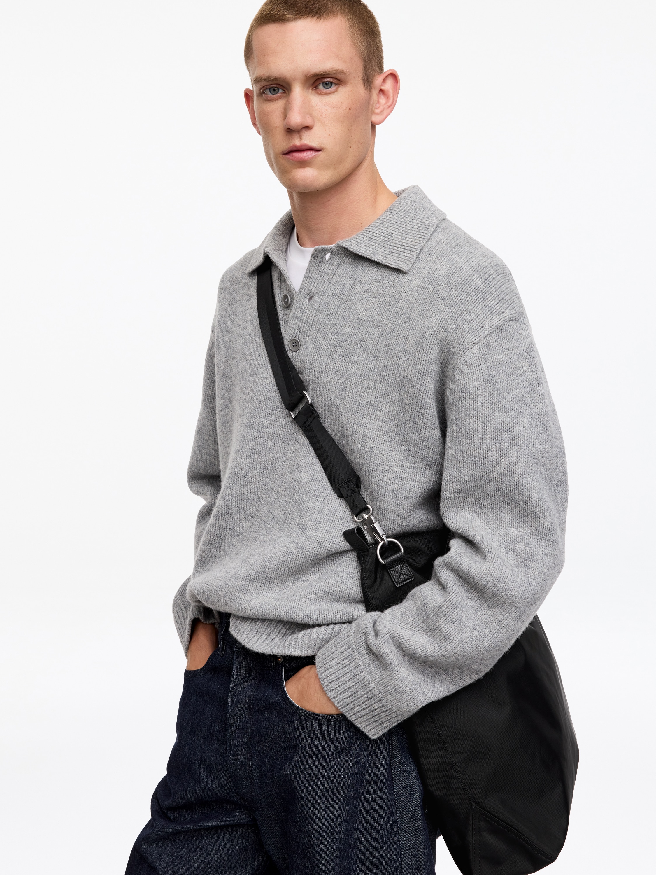 A black nylon tote bag is standing upright in a front view, featuring two textured leather top handles and a zip-top closure. A detachable black webbing shoulder strap hangs from a silver-tone metal clasp on the side.