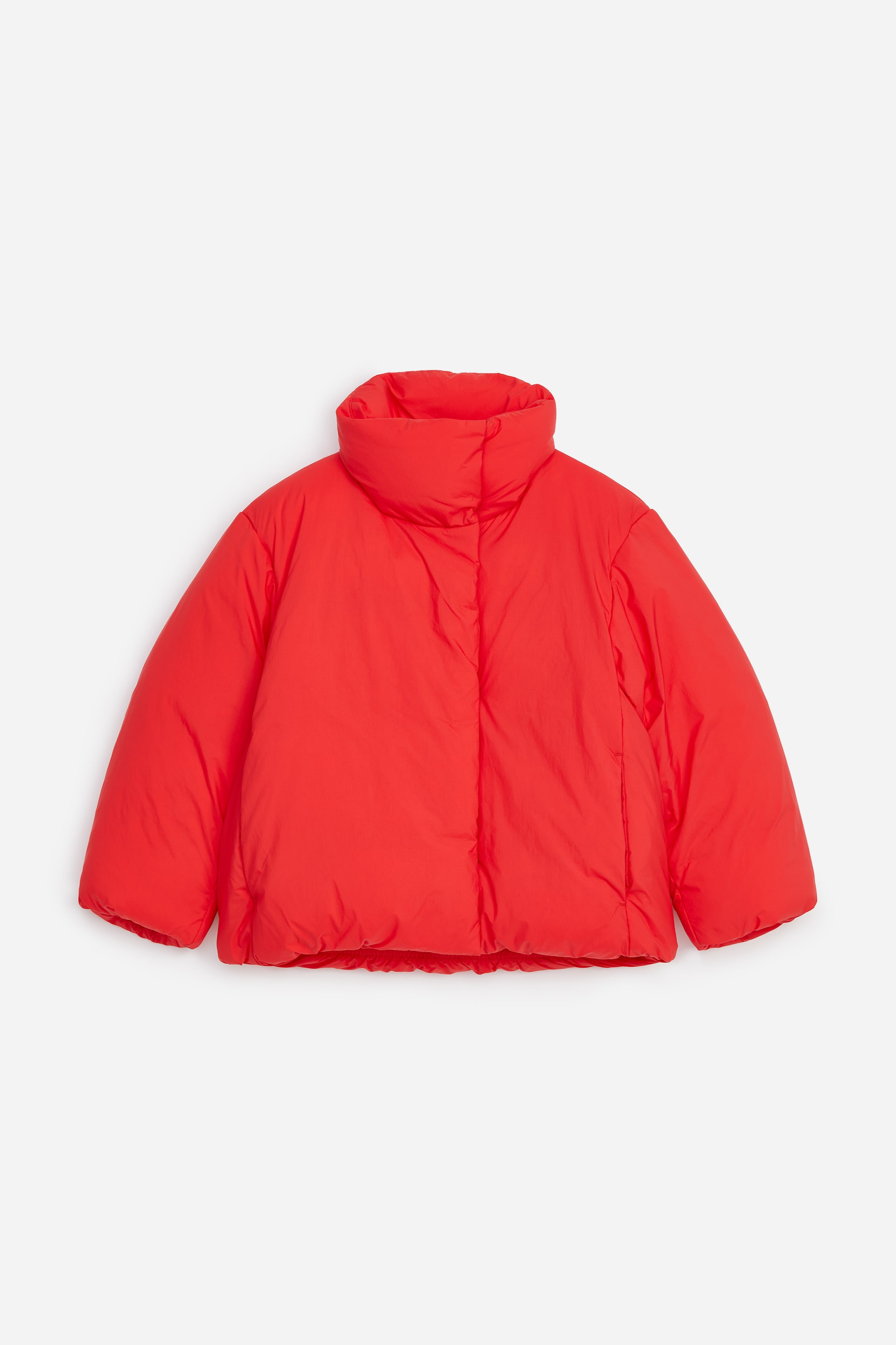 Visualizza immagine più grande: Un piumino rosso acceso è mostrato frontalmente, con un design trapuntato e voluminoso, un colletto alto imbottito e una chiusura frontale nascosta. Il giubbotto presenta maniche lunghe e ampie con polsini puliti e nascosti, oltre a discrete tasche inserite nelle cuciture laterali.