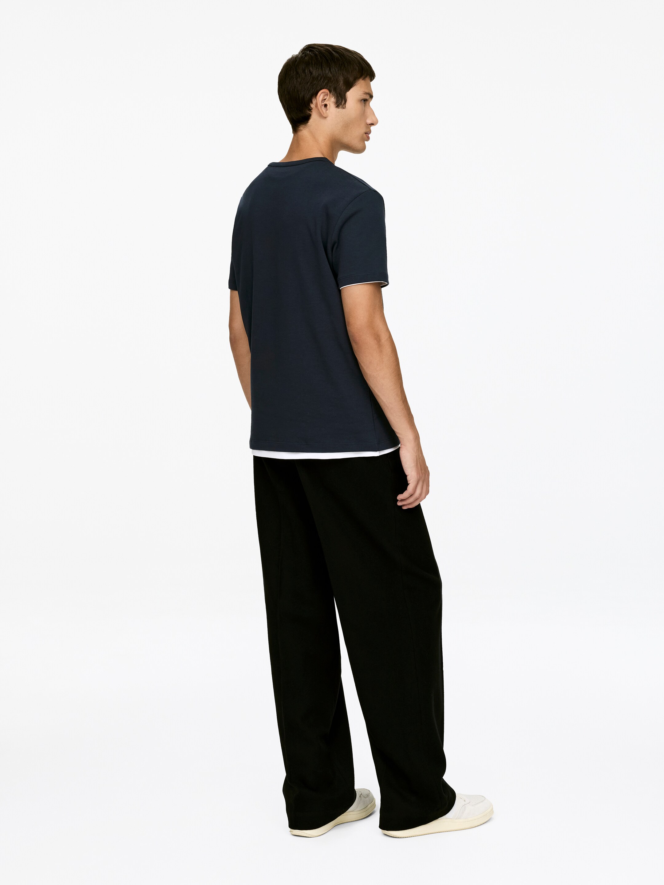Visualizza immagine più grande: Una T-shirt a girocollo blu scuro realizzata in cotone, con una vestibilità aderente al petto e alle braccia, è indossata dalla modella. Ha maniche corte con bordi bianchi ed è sovrapposta a una T-shirt bianca.