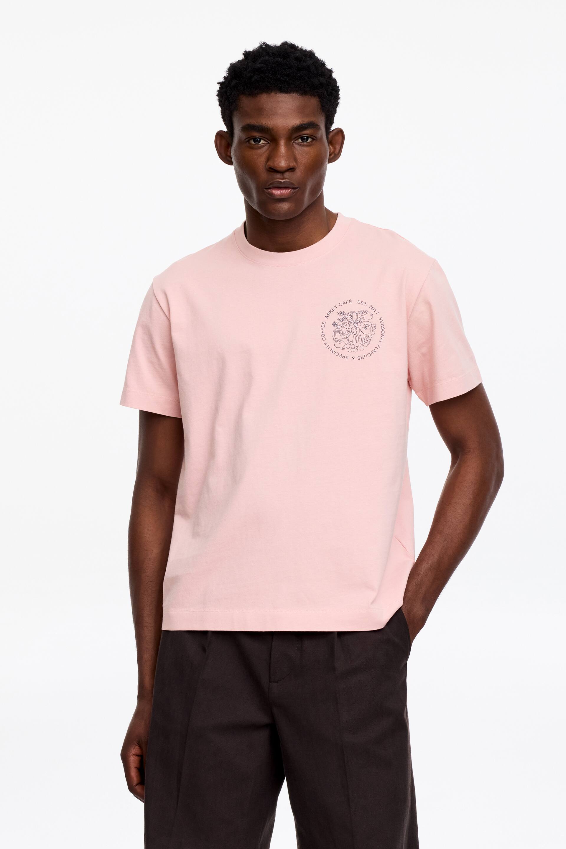 View larger image: A pink short-sleeved t-shirt is facing forward, featuring a crew neck and a circular graphic print on the left chest, displaying a relaxed fit.