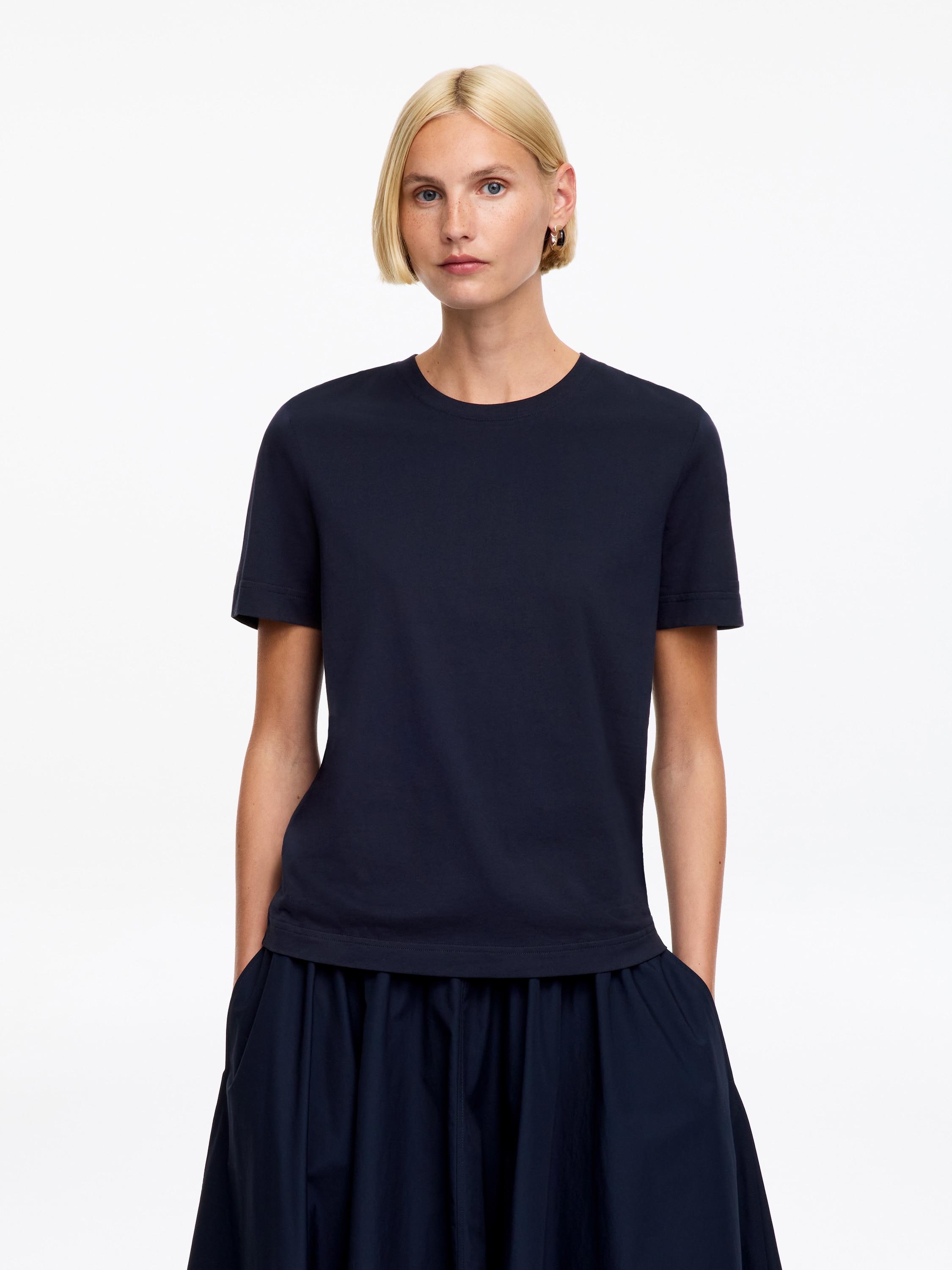 Uma t-shirt azul escura está a apresentar a sua vista FRONTAL, com uma gola redonda canelada e mangas curtas. O tecido aparece liso e uniforme, com uma pequena etiqueta branca visível no interior da parte de trás do pescoço.