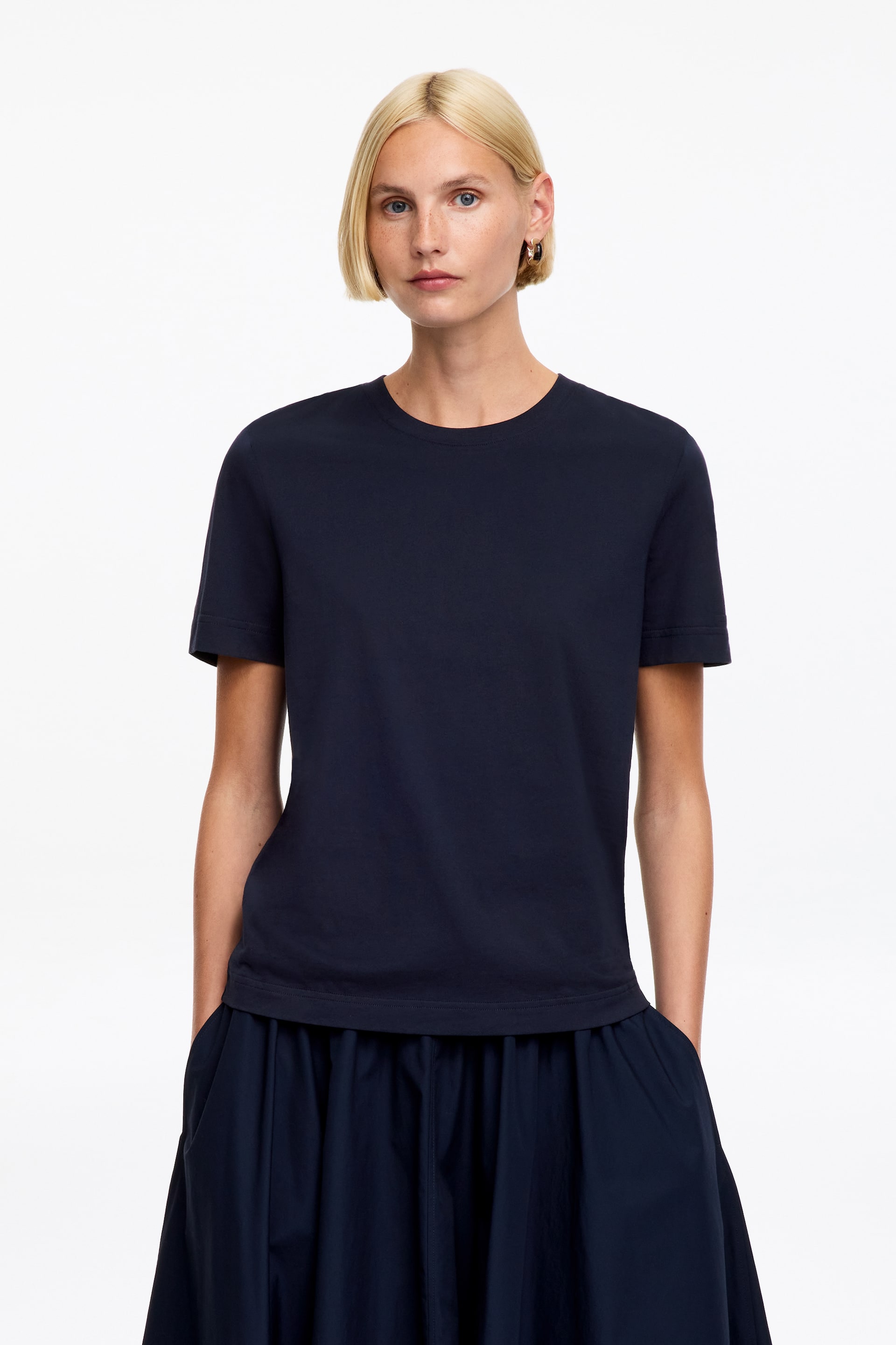 Ver imagem maior: Uma t-shirt azul-marinho apresenta uma gola redonda, mangas curtas e uma bainha reta, oferecendo um corte descontraído ao ser vista de frente.