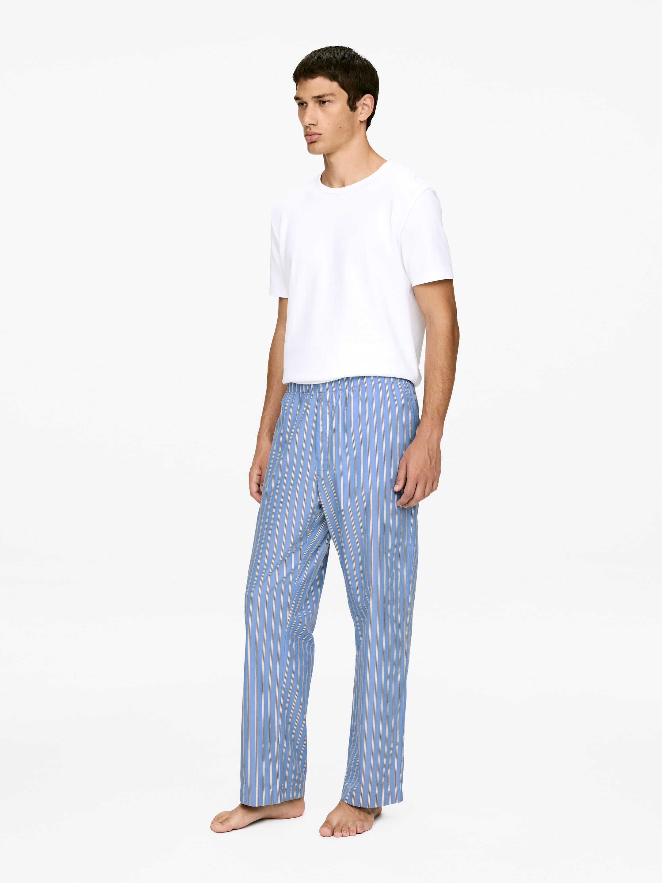 Visualizza immagine più grande: Pantaloni del pigiama blu con sottili strisce verticali beige chiaro sono presentati da un angolo leggermente a destra. I pantaloni presentano una cintura elastica e una vestibilità rilassata con gamba dritta.