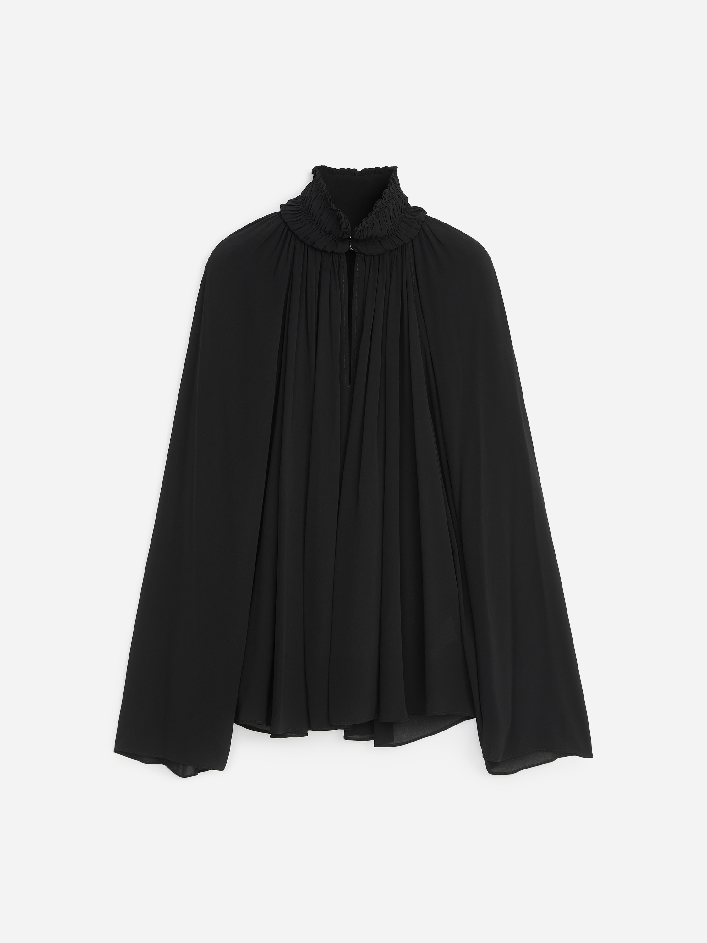 La modella indossa una blusa nera a maniche lunghe, che mette in risalto il suo collo alto con smock, la fessura frontale e il tessuto fluido arricciato che crea una silhouette voluminosa. La blusa è abbinata a jeans grigio scuro, mentre la modella tiene in mano una borsa nera testurizzata.