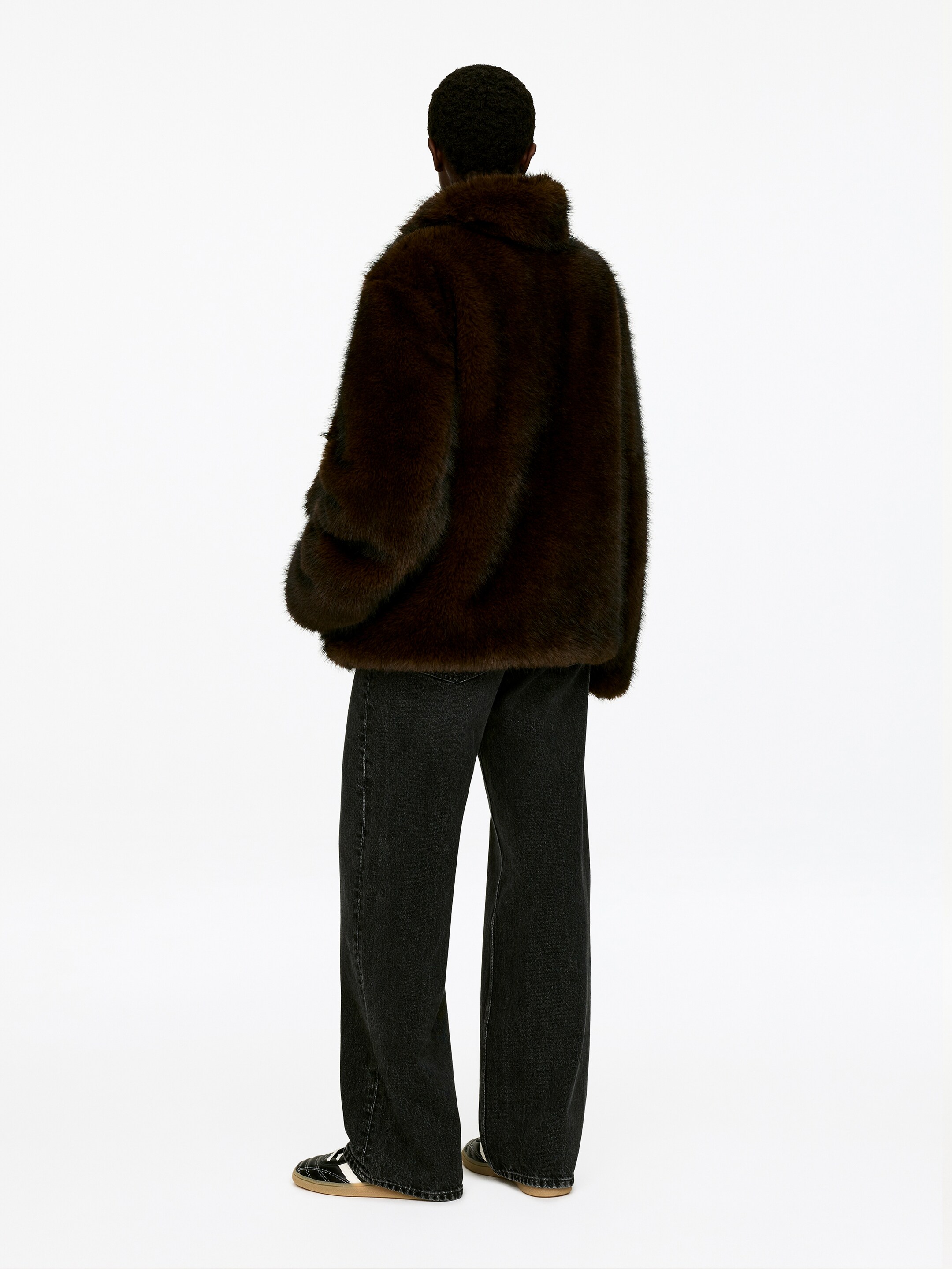Agrandir l'image: Une veste en fausse fourrure brun foncé est montrée de dos. Elle présente un large col moelleux et des manches volumineuses, et recouvre le haut d'un pantalon sombre à jambes larges.