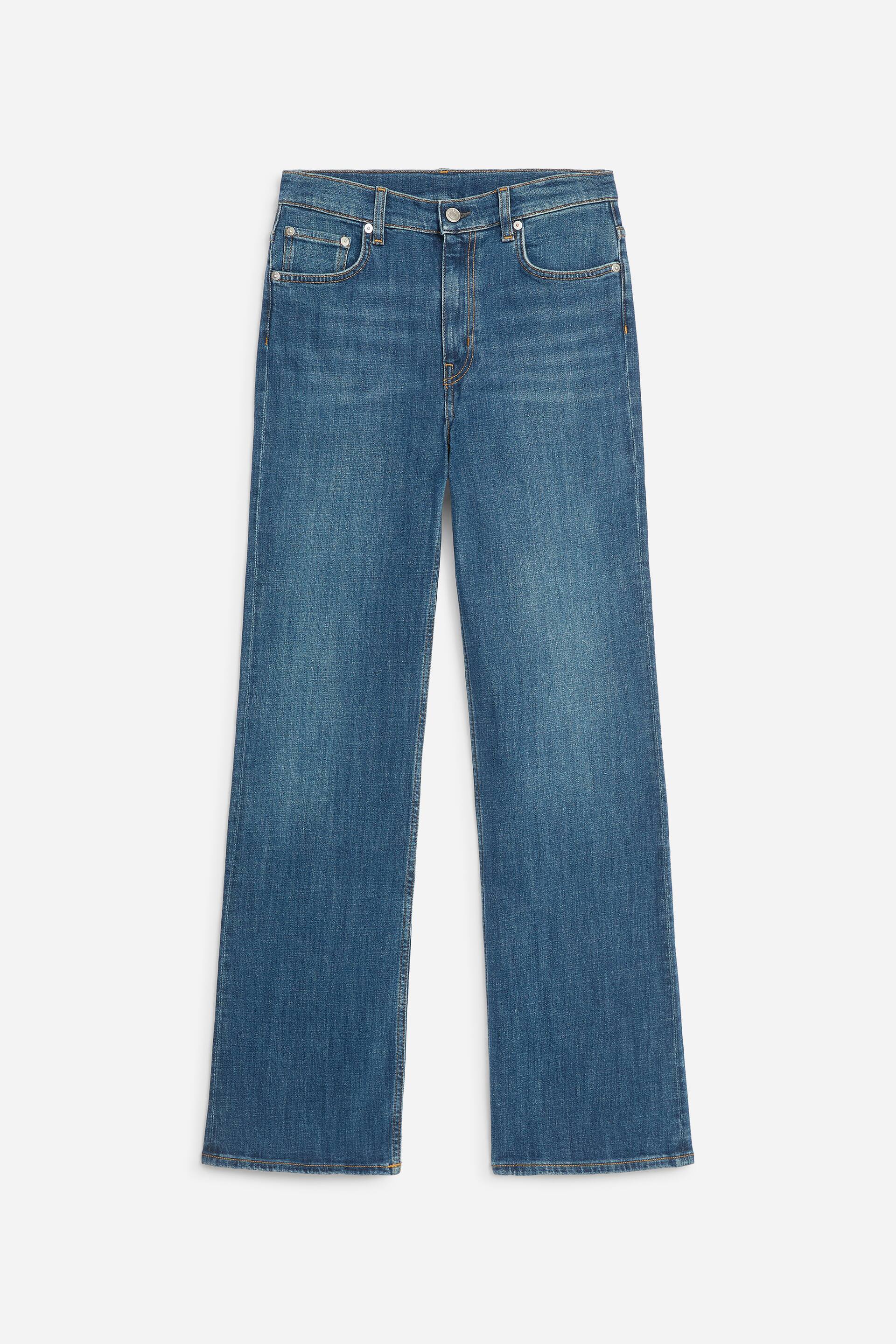 Ver imagen más grande: Estos vaqueros bootcut de tiro alto en un lavado azul medio se presentan en vista frontal, con una construcción clásica de cinco bolsillos, trabillas para cinturón y bragueta con cremallera y cierre de botón. El diseño muestra un corte ajustado en caderas y muslos que se ensancha suavemente hasta una pernera bootcut.