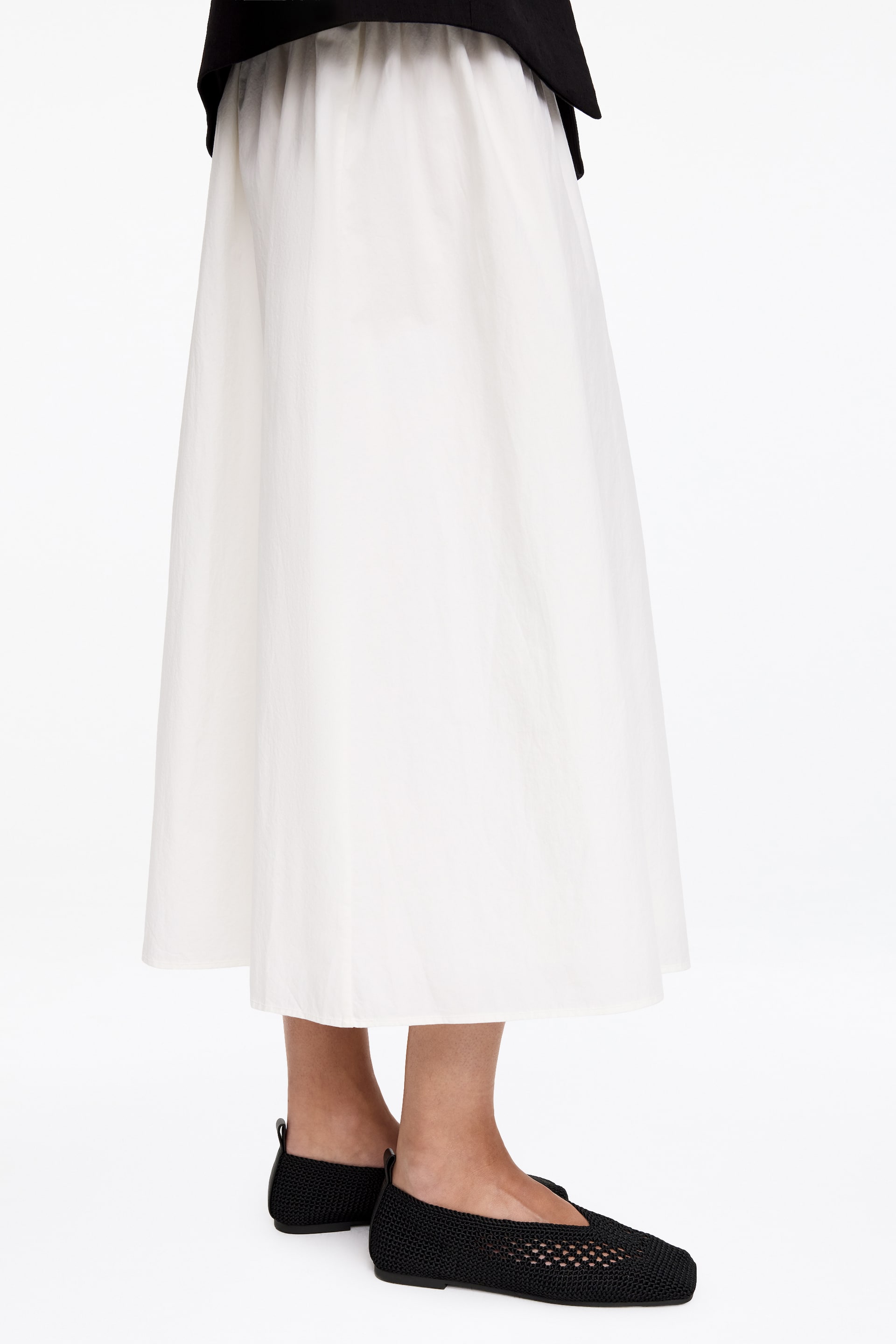 Agrandir l'image: Des ballerines noires en tricot, affichant une silhouette à bout carré et une languette à l'arrière, sont portées par le mannequin.