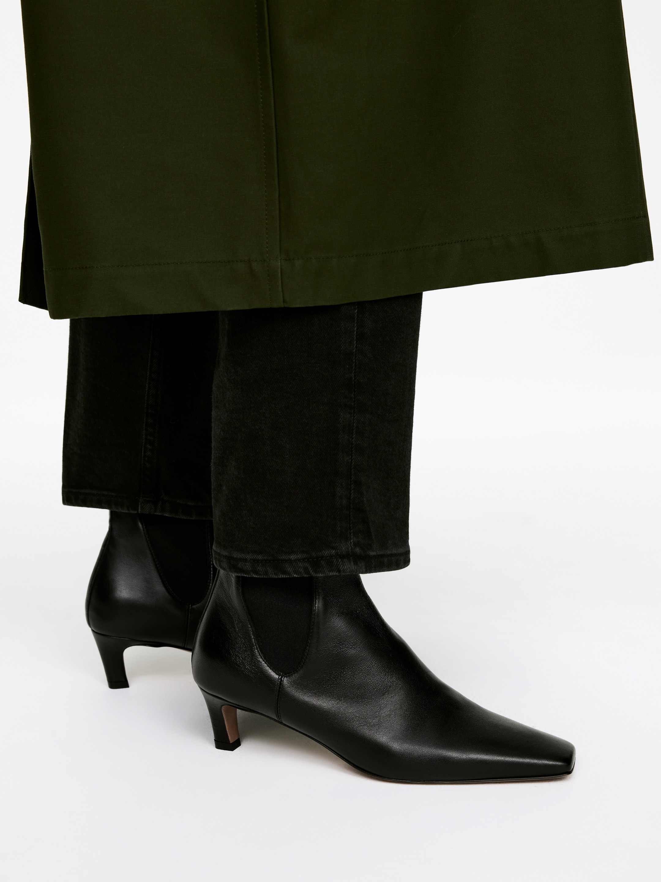 Größeres Bild anzeigen: Schwarze Chelsea-Stiefeletten aus Leder werden getragen, mit quadratischen Zehen und schlanken Kitten-Heels. Die Stiefel werden aus einem leicht frontalen Winkel gezeigt, wobei schwarze Hosen leicht über den Knöcheln zusammenfallen.
