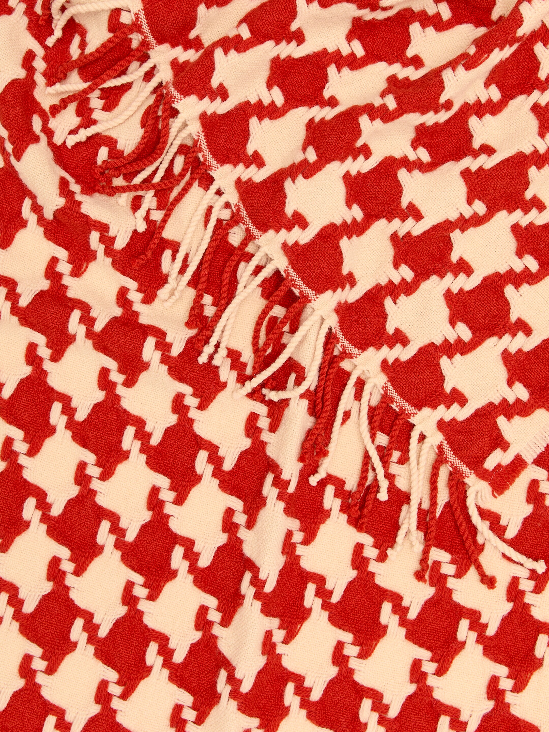 Ver imagen más grande: Un textil rojo y blanco roto presenta un patrón repetido de pata de gallo y bordes con flecos visibles.