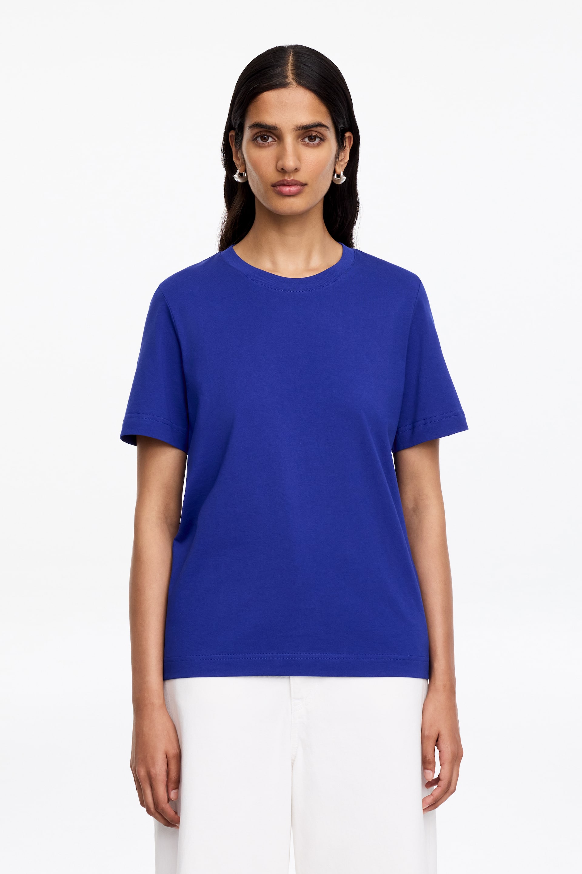 Agrandir l'image: Un t-shirt bleu royal avec un col rond côtelé et des manches courtes est porté par le mannequin. Il est associé à un pantalon blanc.