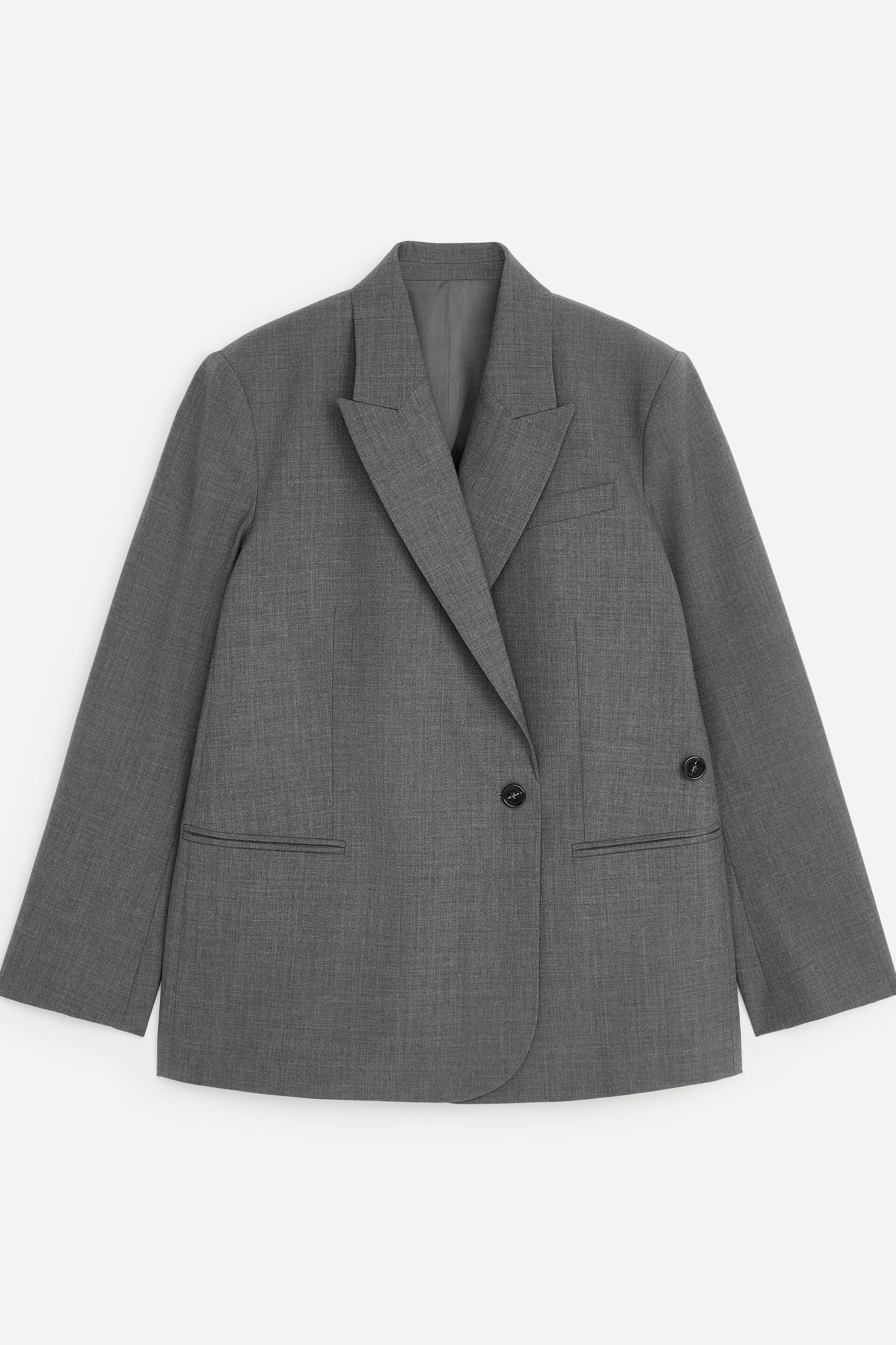 Grotere afbeelding bekijken: De grijze blazer ligt plat en recht naar voren gericht, met brede revers met inkeping en een sluiting met één knoop en een brede overlappende voorkant. Het ontwerp heeft één zichtbaar paspelzakje op de borst, twee klepzakken aan de onderzijde van de voorkant en twee kleine knopen op elke manchet.