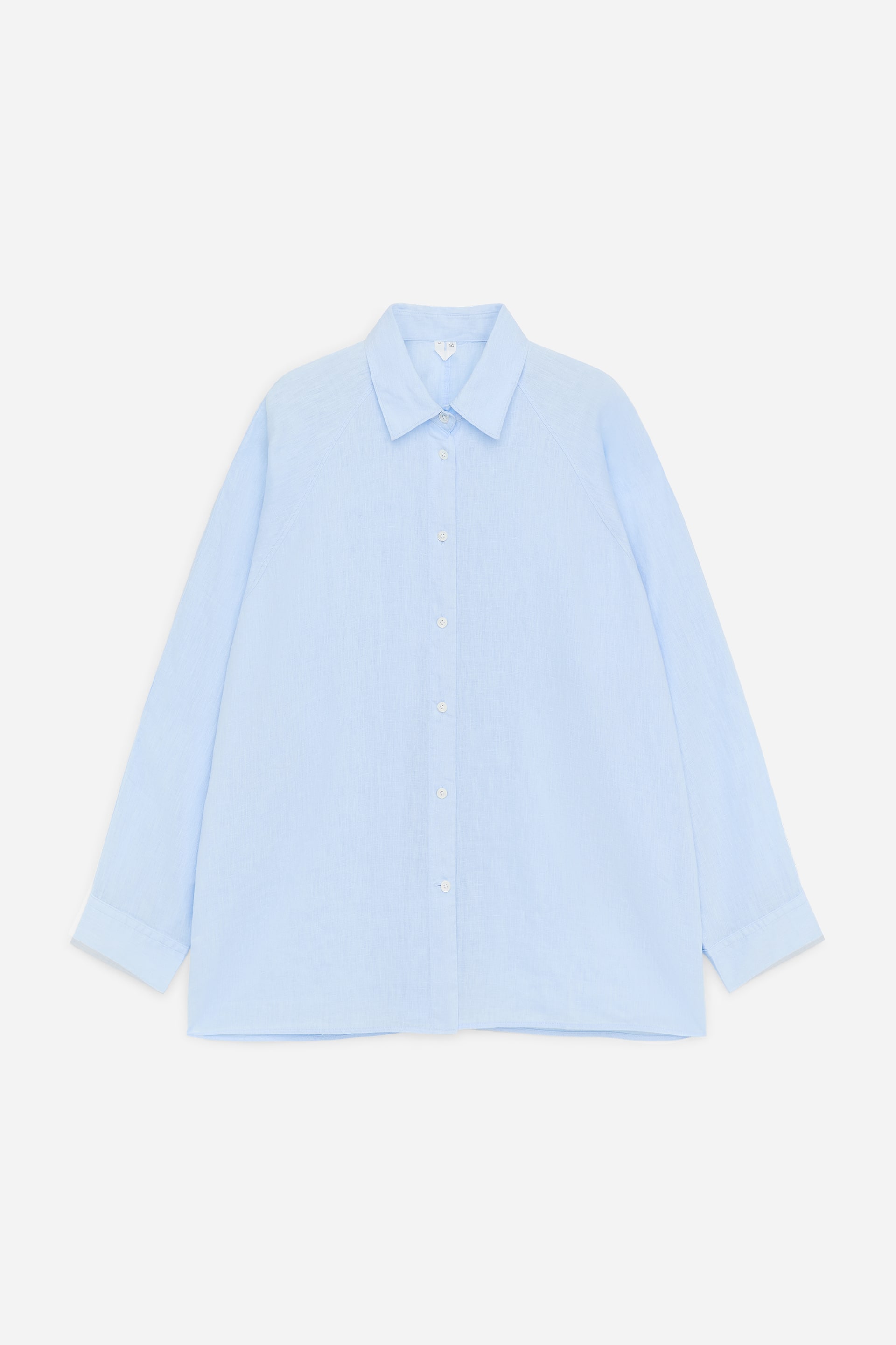 Agrandir l'image: Une chemise en lin bleu clair est présentée de face, avec une coupe ample, des manches raglan et un col pointu. Une patte de boutonnage complète avec des boutons blancs descend au centre, et le tissu présente un tissage subtilement texturé.