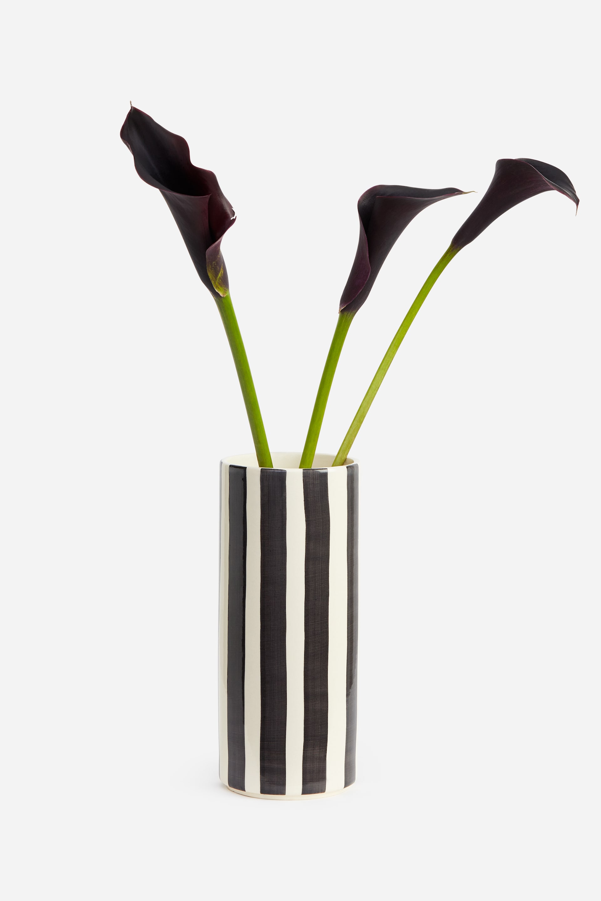 Visualizza l'immagine ingrandita: Un vaso cilindrico in gres smaltato con strisce verticali nere e bianco sporco è in posizione verticale e contiene tre calle di colore viola scuro con steli verdi. Il vaso presenta una finitura liscia e lucida con una silhouette pulita e dai bordi netti.