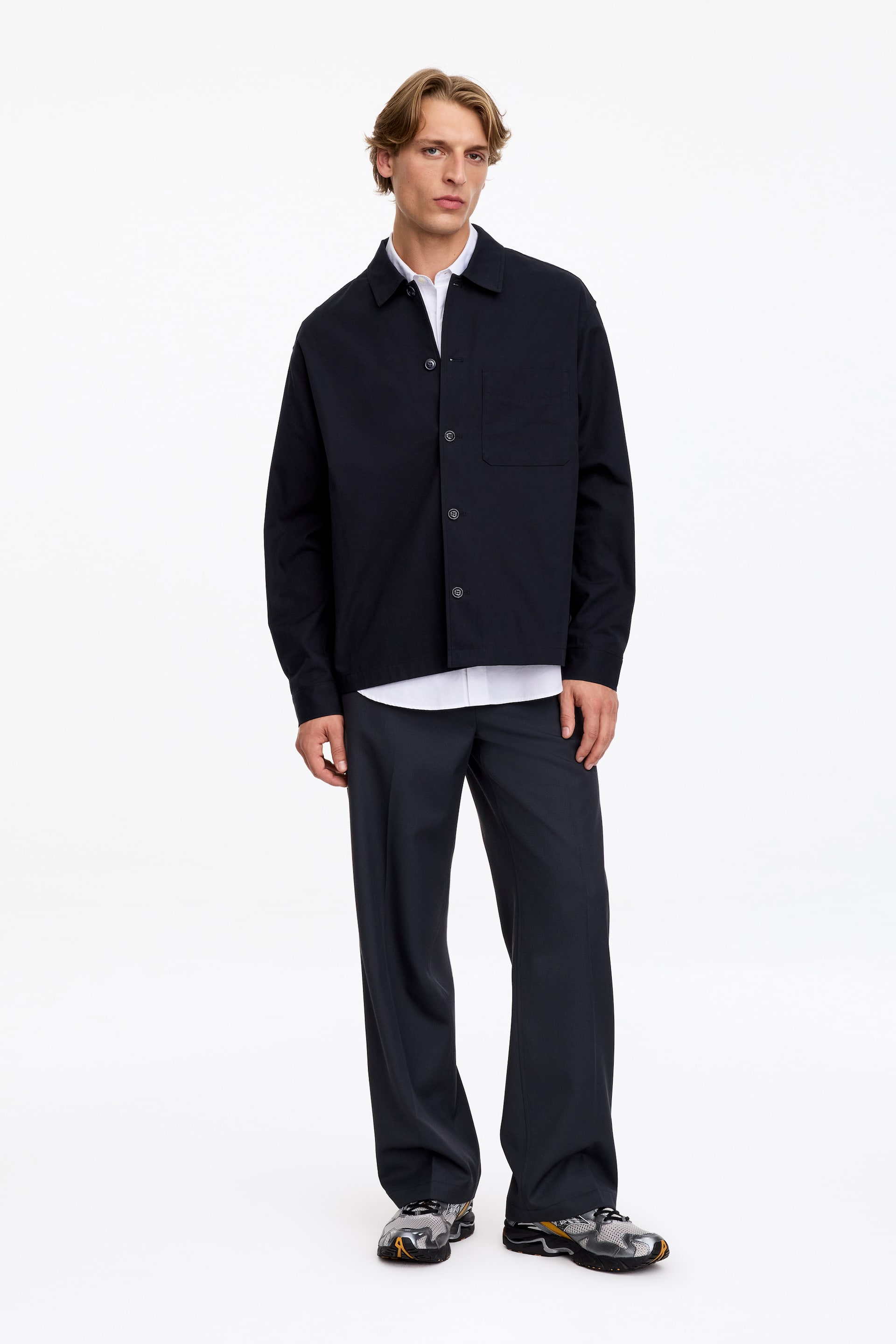 Grotere afbeelding bekijken: Het model draagt een donker marineblauwe overshirt, gelaagd over een wit hemd met kraag en gecombineerd met een donkere broek. De overshirt met lange mouwen heeft een reguliere kraag, een knoopsluiting vooraan en een enkele opgestikte borstzak.