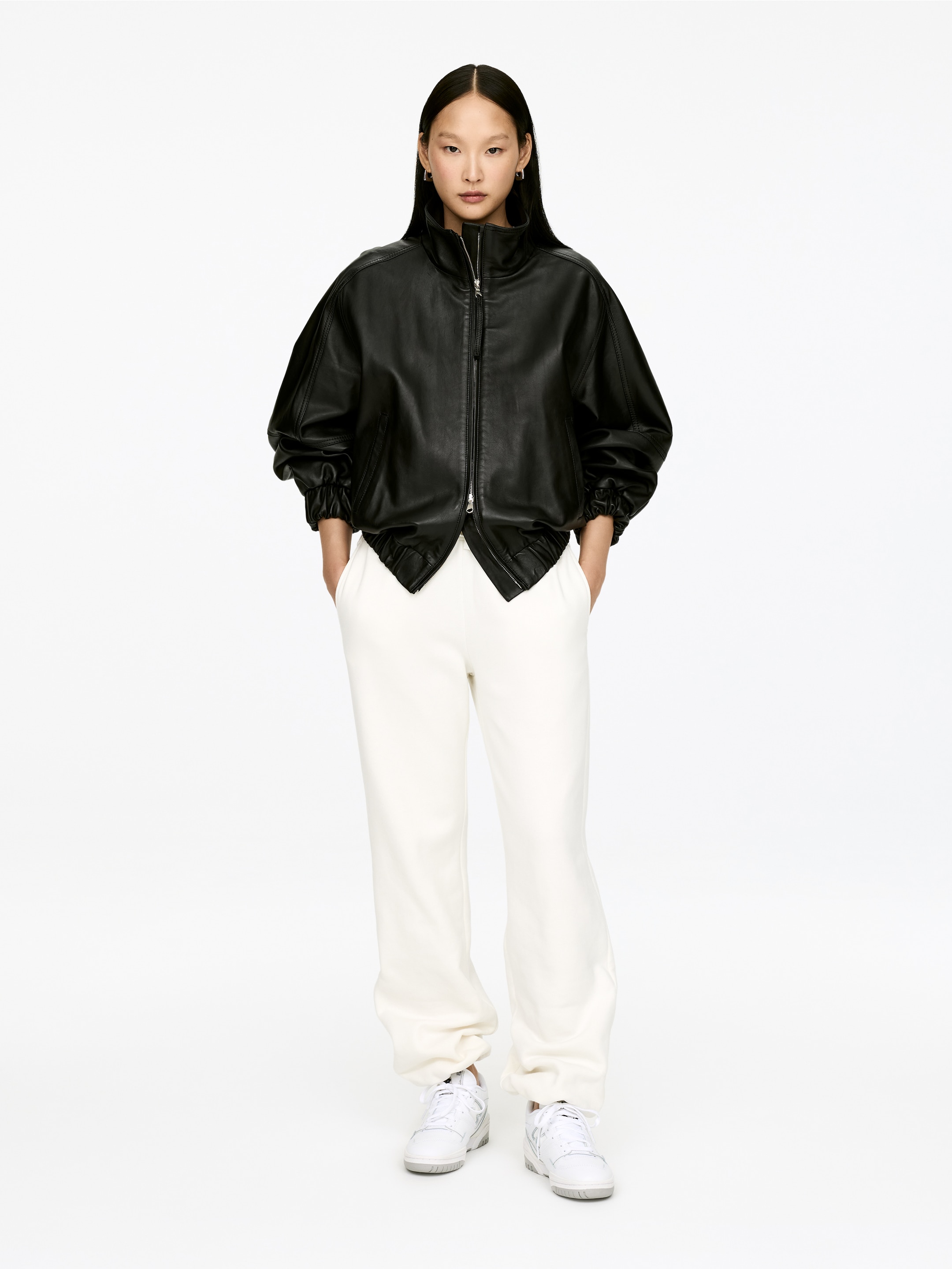 Agrandir l'image: Une veste bomber en cuir noir est présentée en vue de face. Elle se caractérise par un col montant, une fermeture frontale zippée de couleur argentée, et des manches volumineuses avec des poignets et un ourlet élastiqués et froncés.