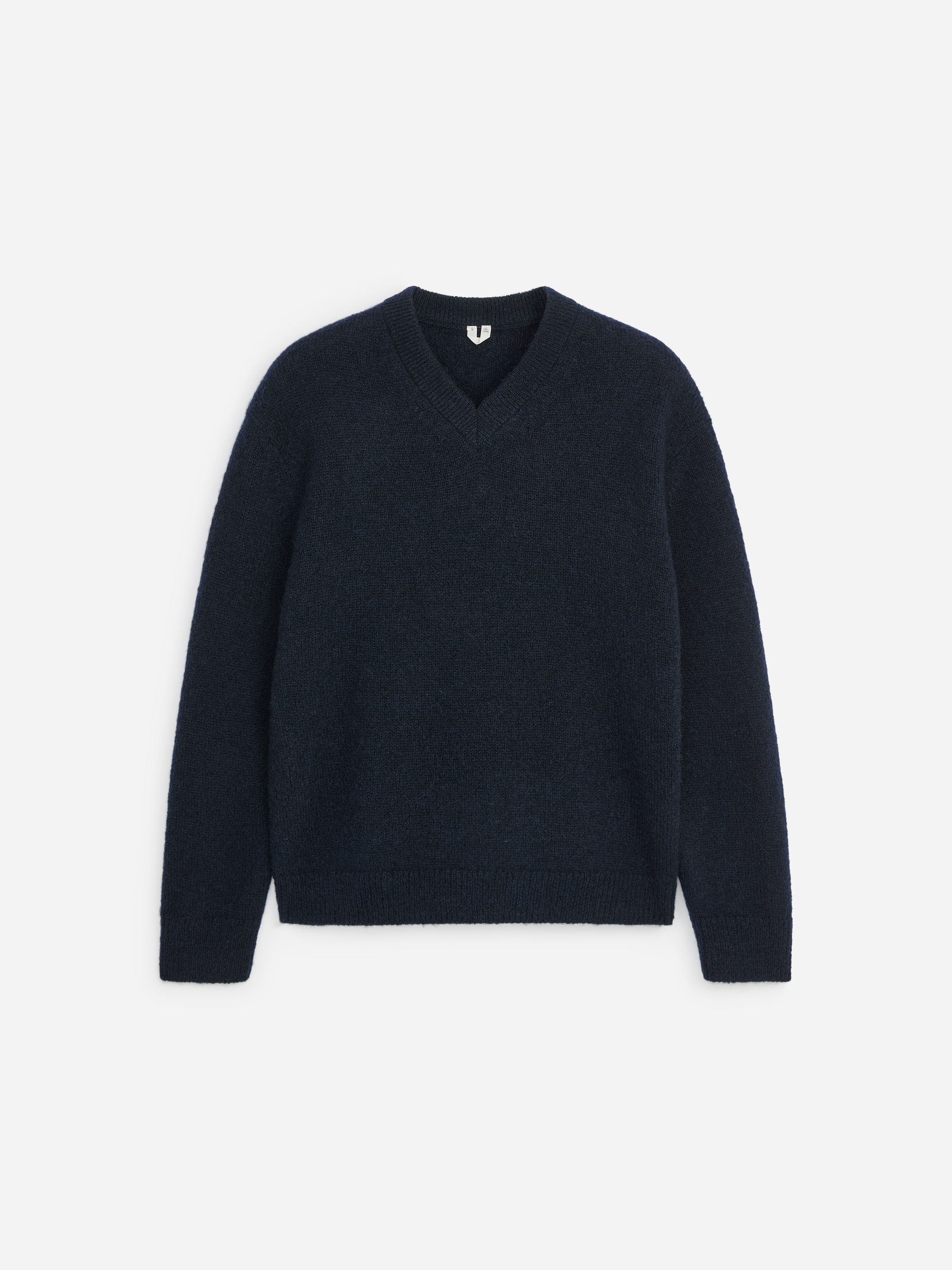 En mørk marineblå, struktureret striktrøje med V-udskæring bæres af modellen, lagdelt over en blå- og hvidstribet skjorte med knapper og en hvid T-shirt. Trøjen har en afslappet pasform med ribkanter ved ærmer og søm og er stylet med mørkebrune bukser.