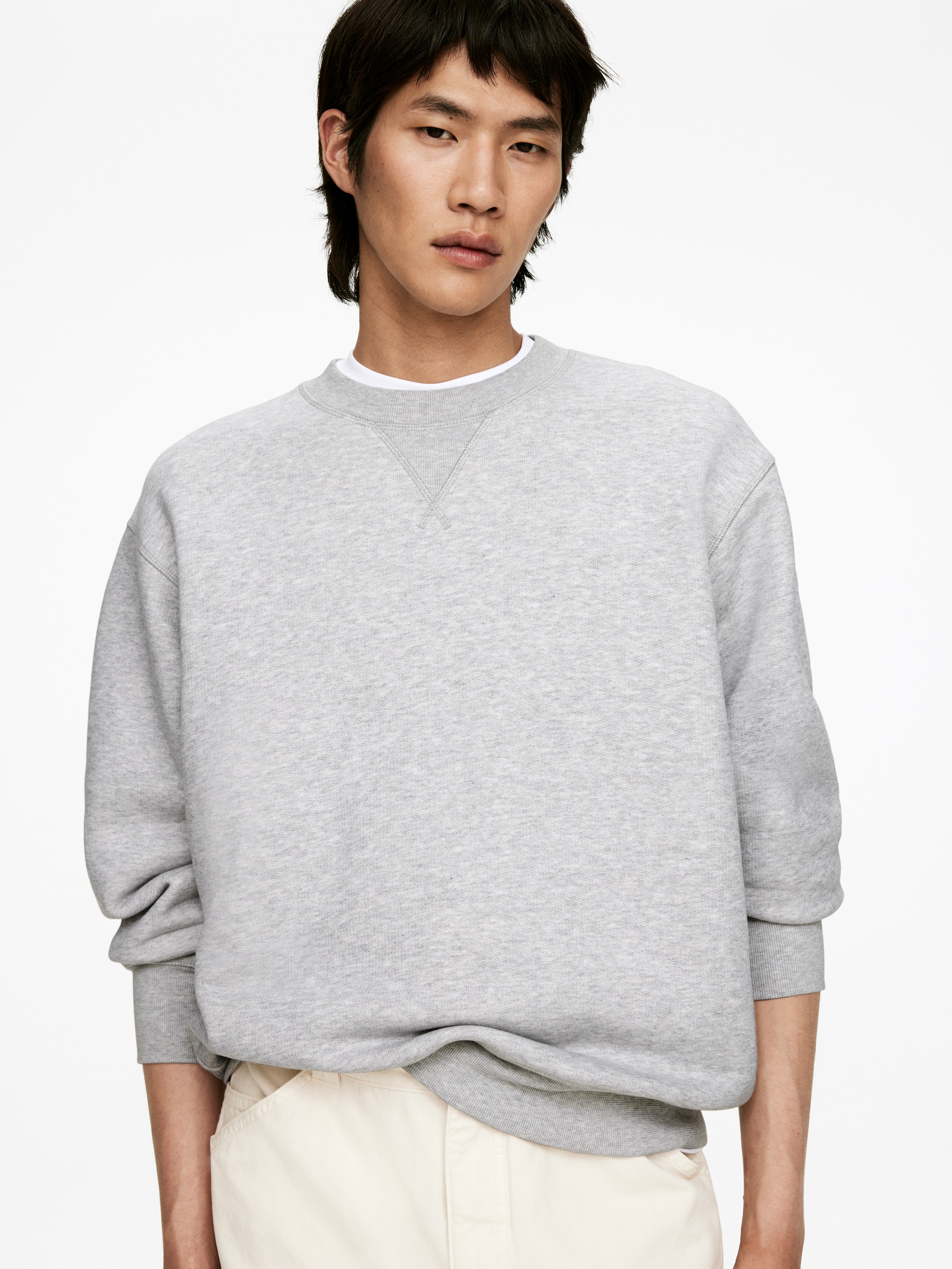 Größeres Bild anzeigen: Ein hellgraues Sweatshirt mit Rundhalsausschnitt präsentiert eine entspannte Passform, mit einem gerippten Kragen mit V-Stich-Detail und gerippten Bündchen. Ein weißes T-Shirt ist sichtbar unter dem Ausschnitt geschichtet.