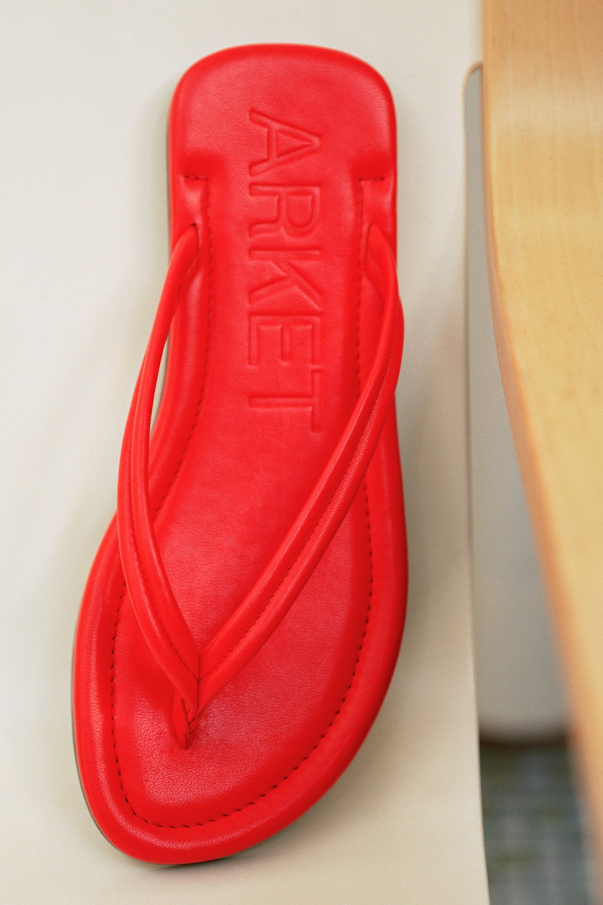 Se større billede: En rød tåsandal ligger fladt, og fremviser en polstret fodseng med præget "ARKET" branding. Den har slanke stropper og synlig syning langs kanten.