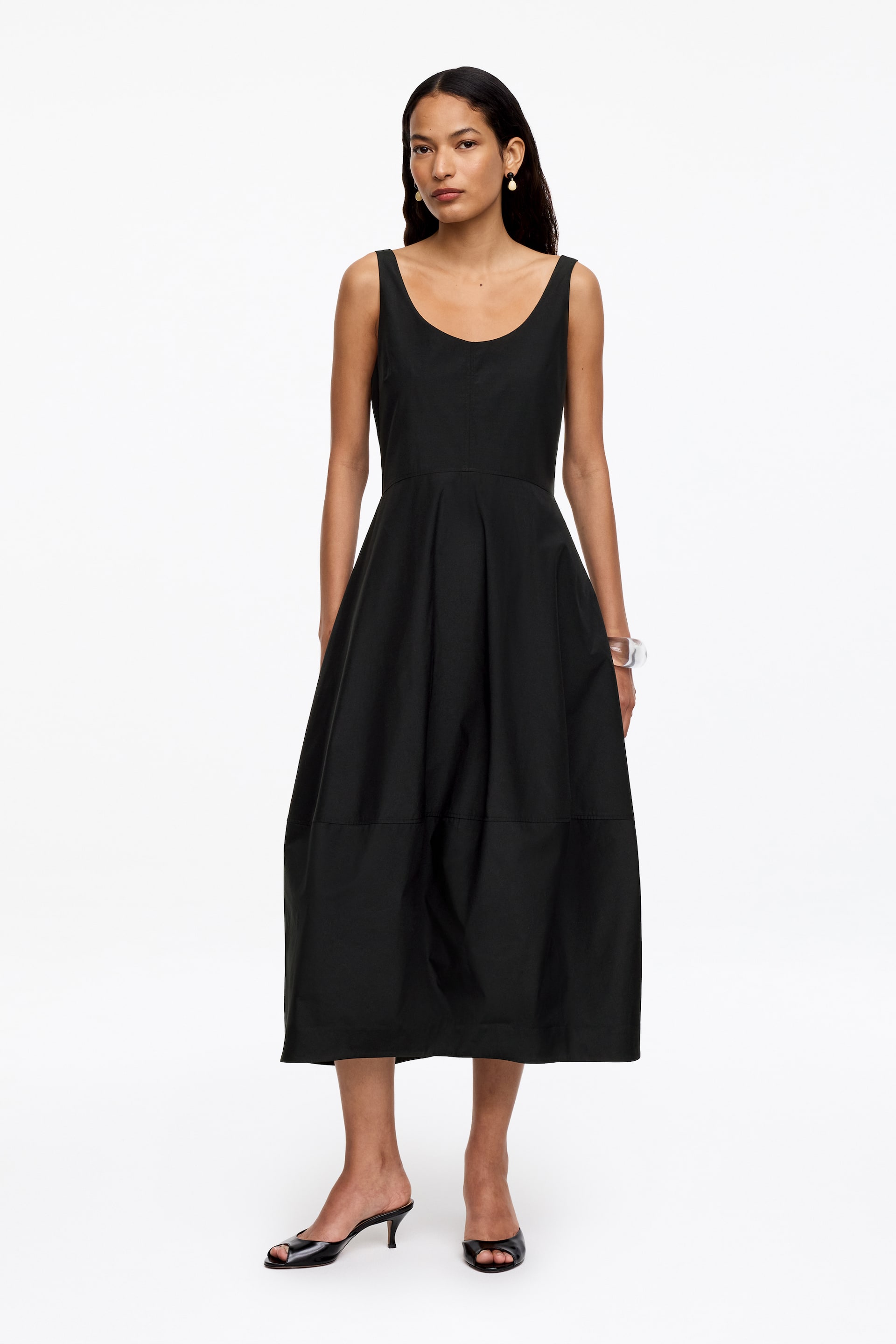 Zobacz większy obraz: Czarna sukienka bez rękawów charakteryzuje się okrągłym dekoltem, dopasowaną górą i pełną, rozkloszowaną spódnicą w kształcie litery A. Spódnica jest widocznie panelowana z poziomym szwem blisko brzegu i sięga długości midi.