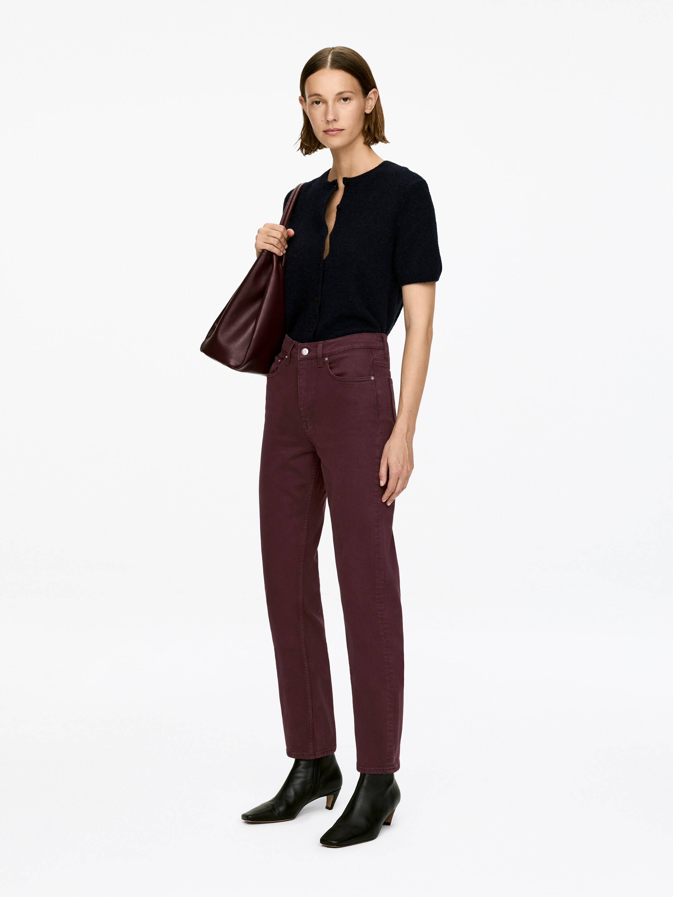 Vezi imaginea mai mare: Blugii JADE CROPPED, într-o nuanță de roșu intens, sunt purtați de model. Blugii prezintă o talie de înălțime medie, un fermoar vizibil, o croială slim și picioare conice, tăiate scurt, care sunt asortate cu botine negre.
