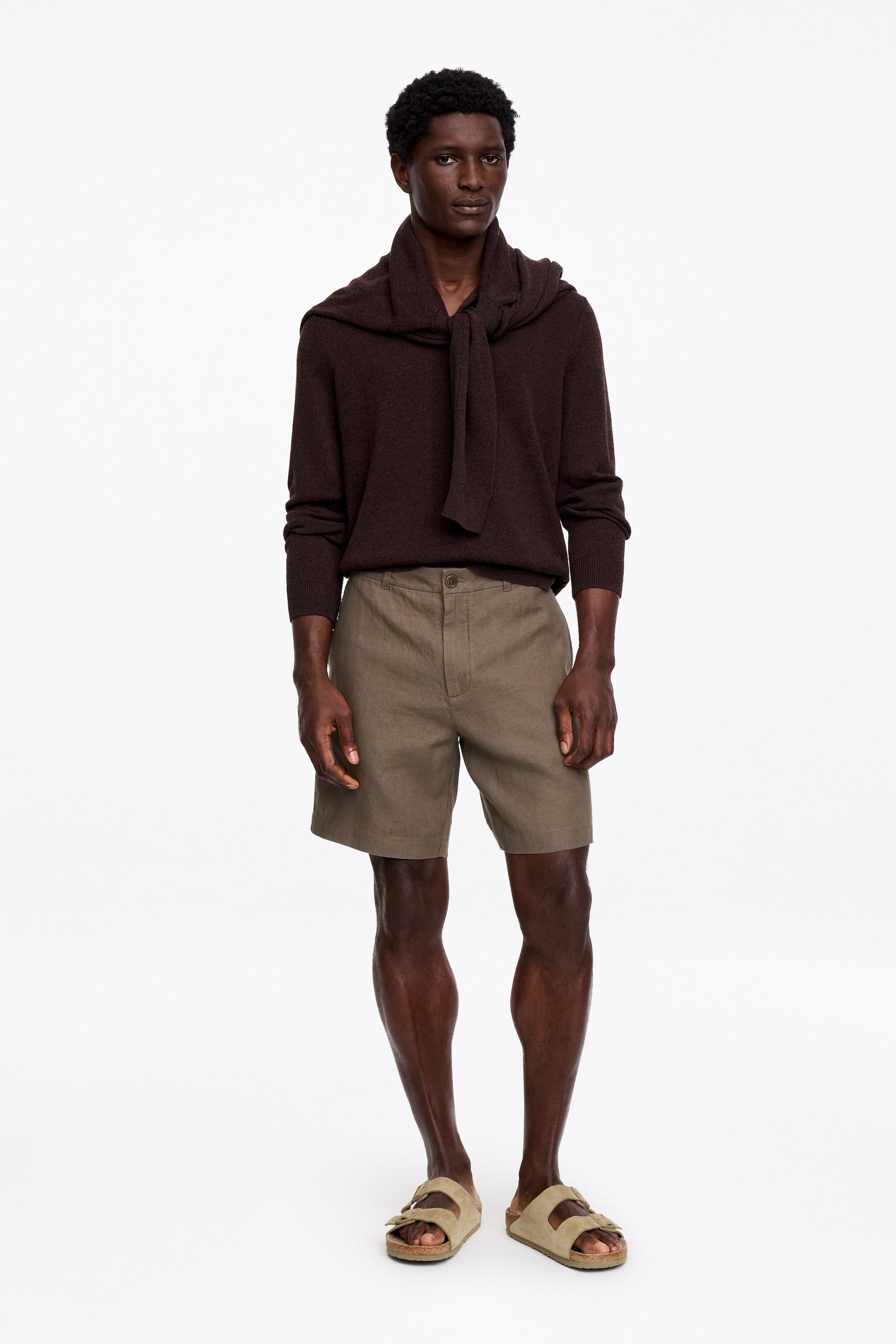 Visualizza immagine più grande: Pantaloncini in lino verde oliva, tagliati a metà coscia, indossati dal modello. Questi pantaloncini a vestibilità regolare presentano una chiusura con zip e bottone e tasche frontali inclinate.