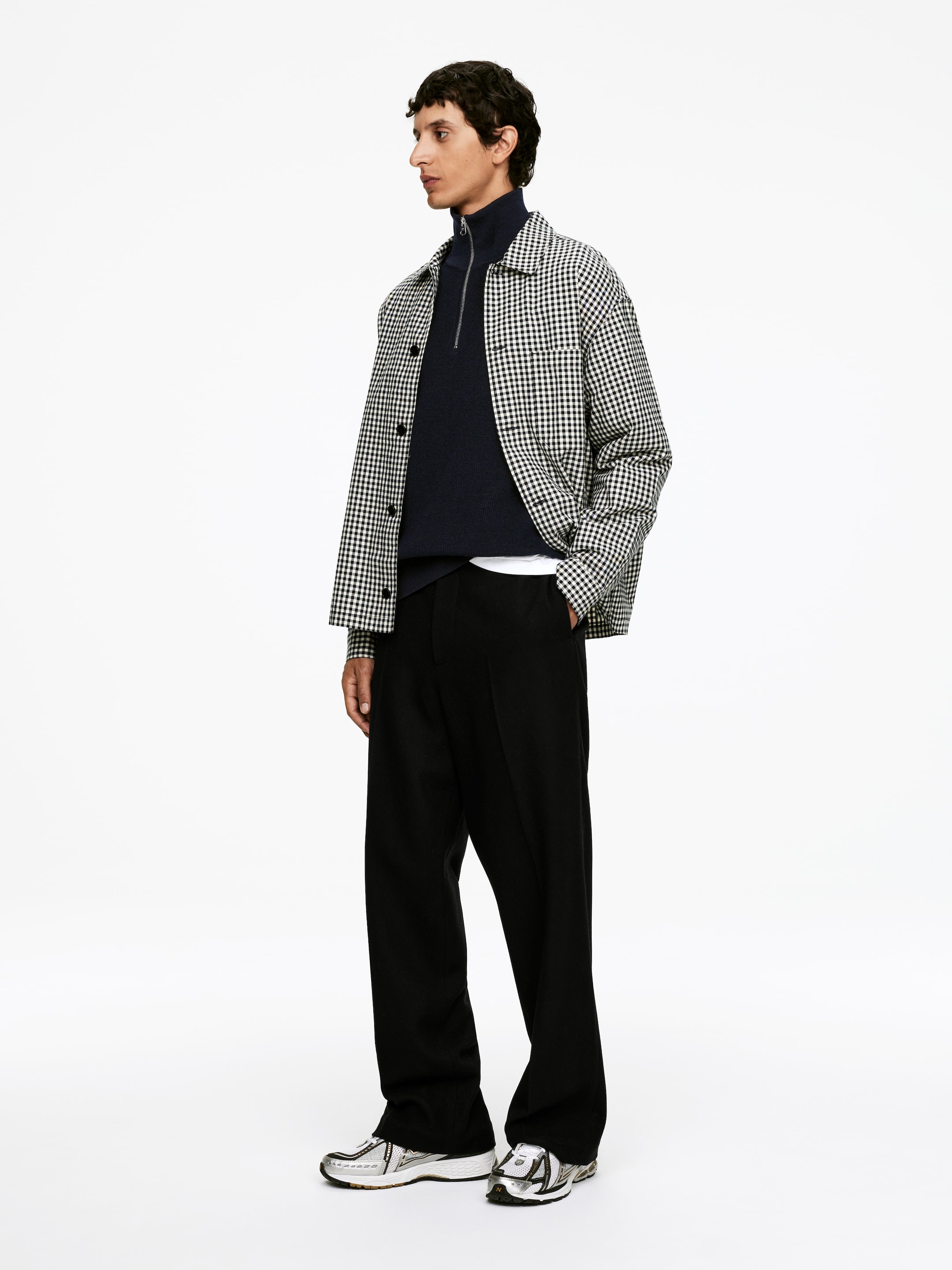 Visualizza immagine più grande: Un maglione a mezza zip in lana e cotone blu scuro è indossato dal modello. La sua chiusura a mezza zip argentata è parzialmente aperta, ed è stratificato sopra una t-shirt bianca e sotto una giacca con colletto a quadretti bianco e nero.
