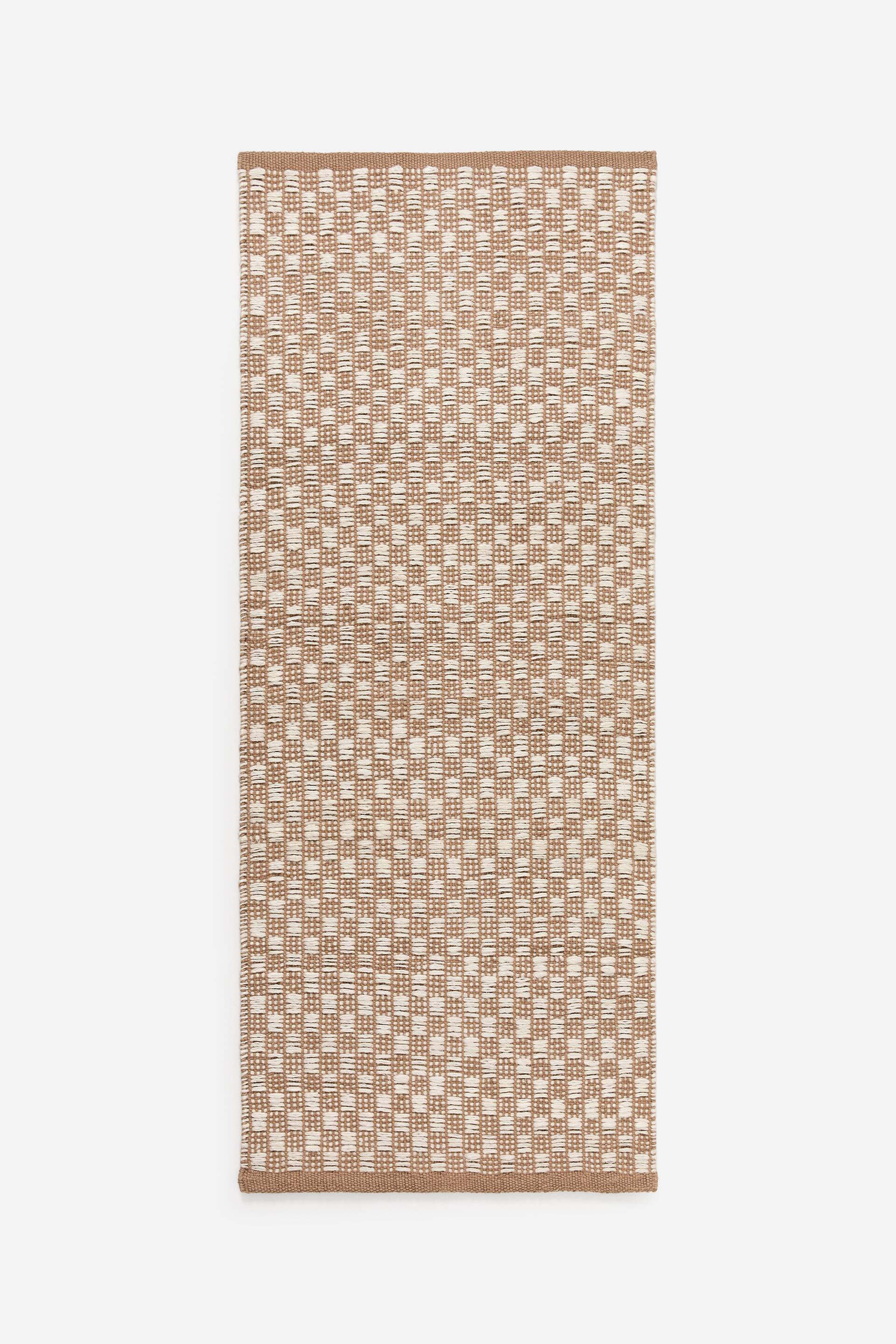 Agrandir l'image: Un chemin de table rectangulaire en textile tissé présente un motif texturé, formé par de petits segments rectangulaires blanc cassé entrelacés dans une grille brun clair. Il est doté de bords finis d'un brun clair uni le long de ses côtés courts.
