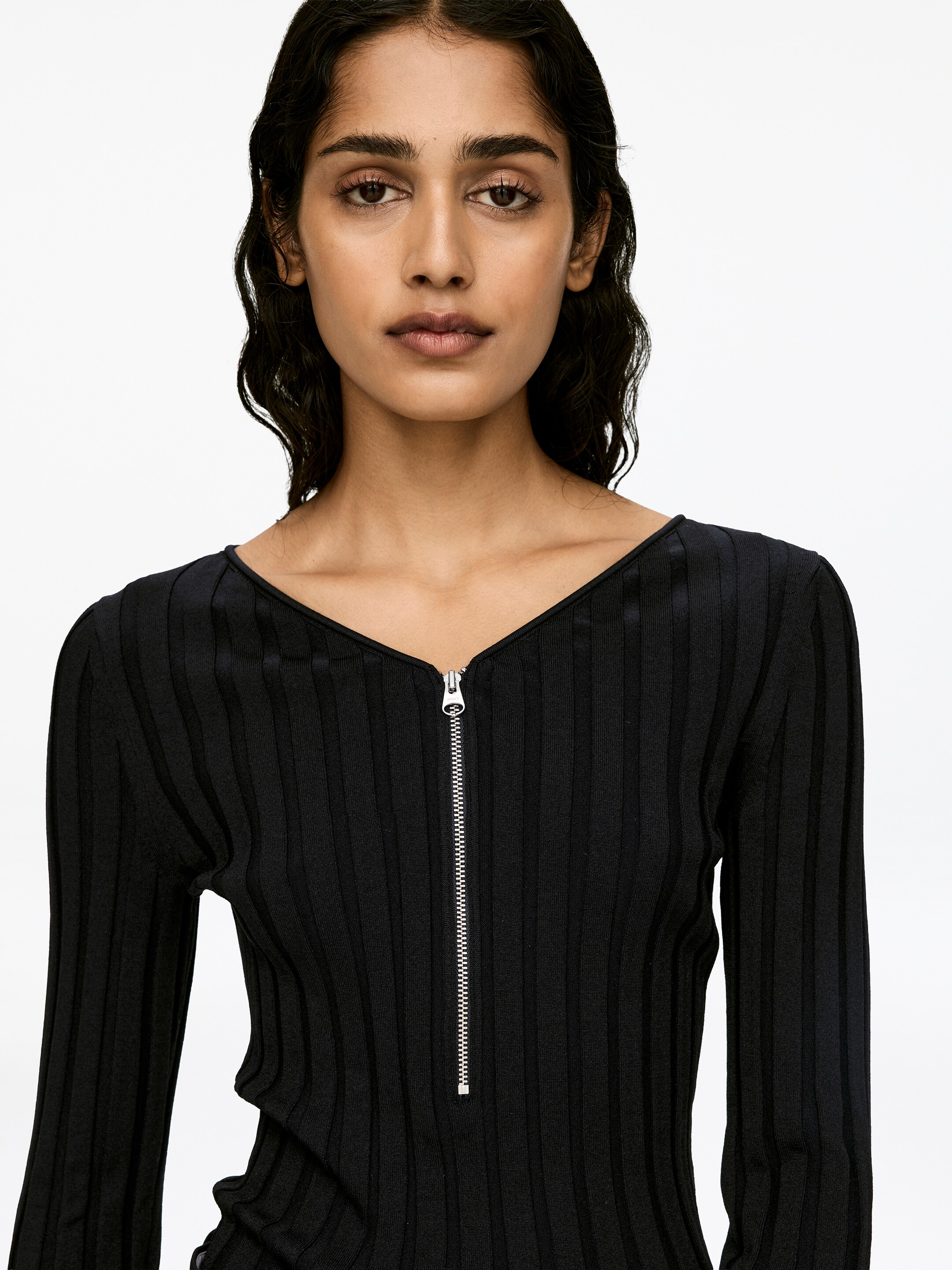 View larger image: A black long-sleeved, rib-knit jumper is being worn by the model. The slim-fit jumper features a silver half-zip at the center front, which is partially unzipped, forming a V-neck.