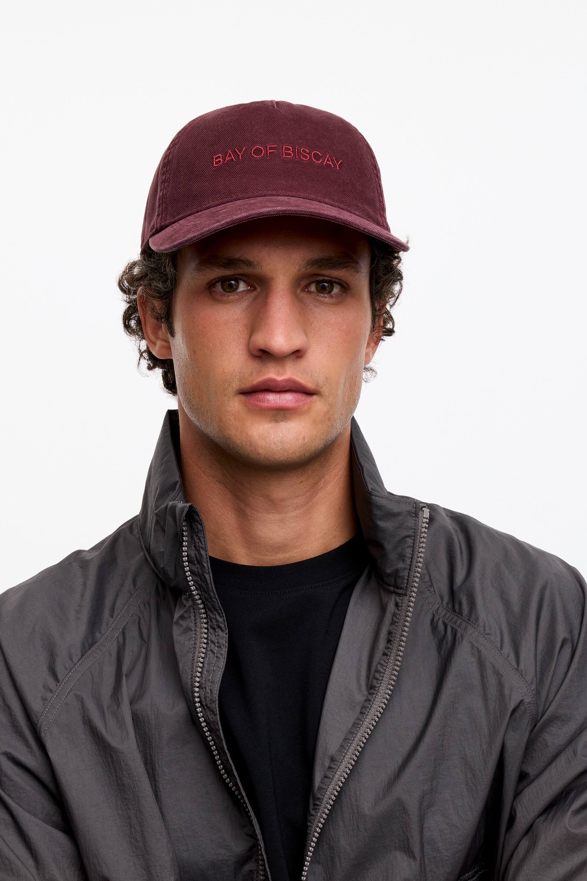 Visa större bild: En vinröd baseballkeps i tvättad bomullstwill bärs, med "BAY OF BISCAY" broderat i röda versaler över framsidan.