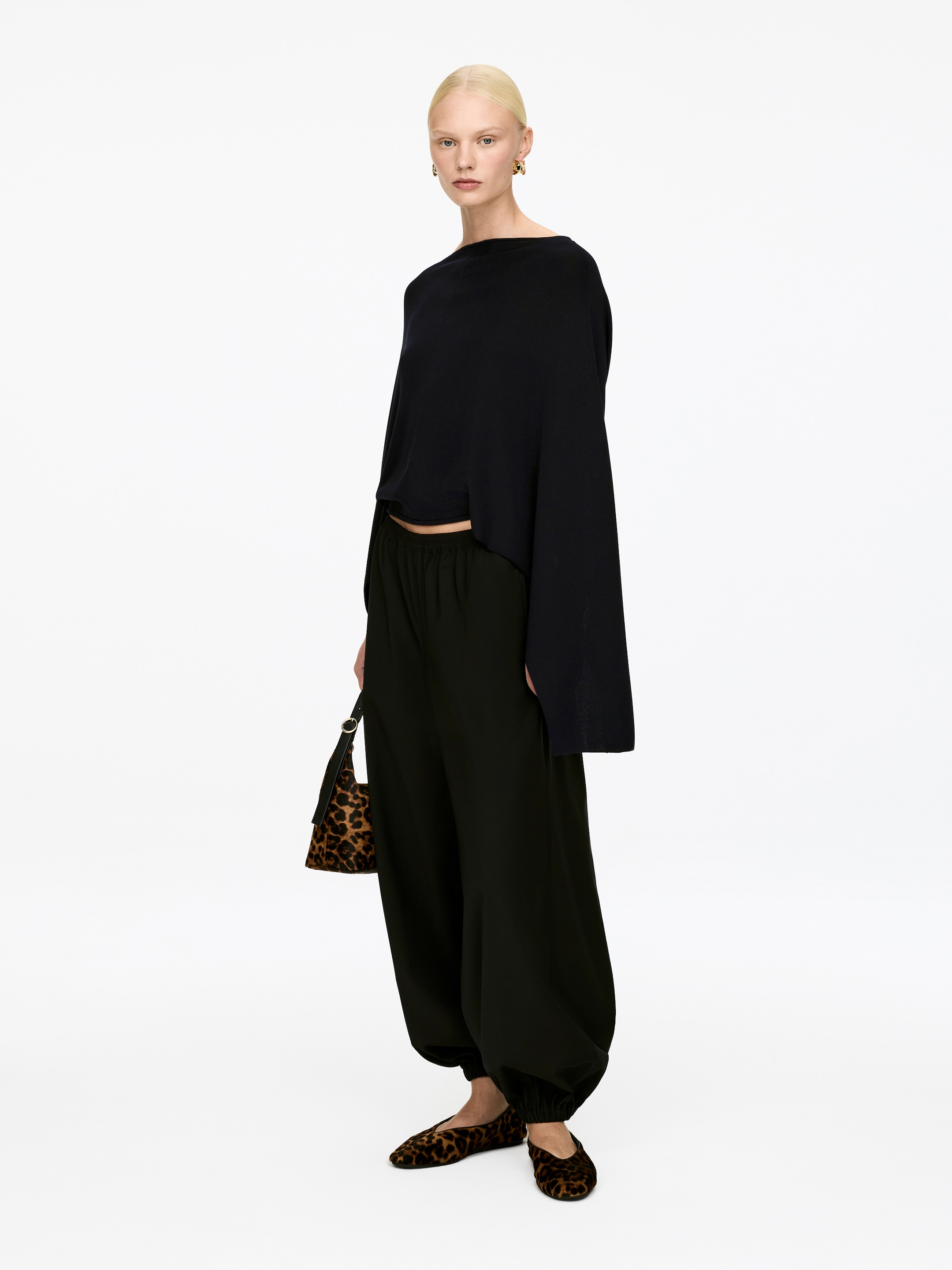 Agrandir l'image: Un haut noir à col large présente des manches longues et larges ainsi qu'une silhouette légèrement raccourcie et fluide, présentant son devant et ses côtés. Un pantalon vert foncé arbore une coupe décontractée et volumineuse avec une taille élastiquée et des chevilles froncées, présentant également leur devant et leurs côtés.