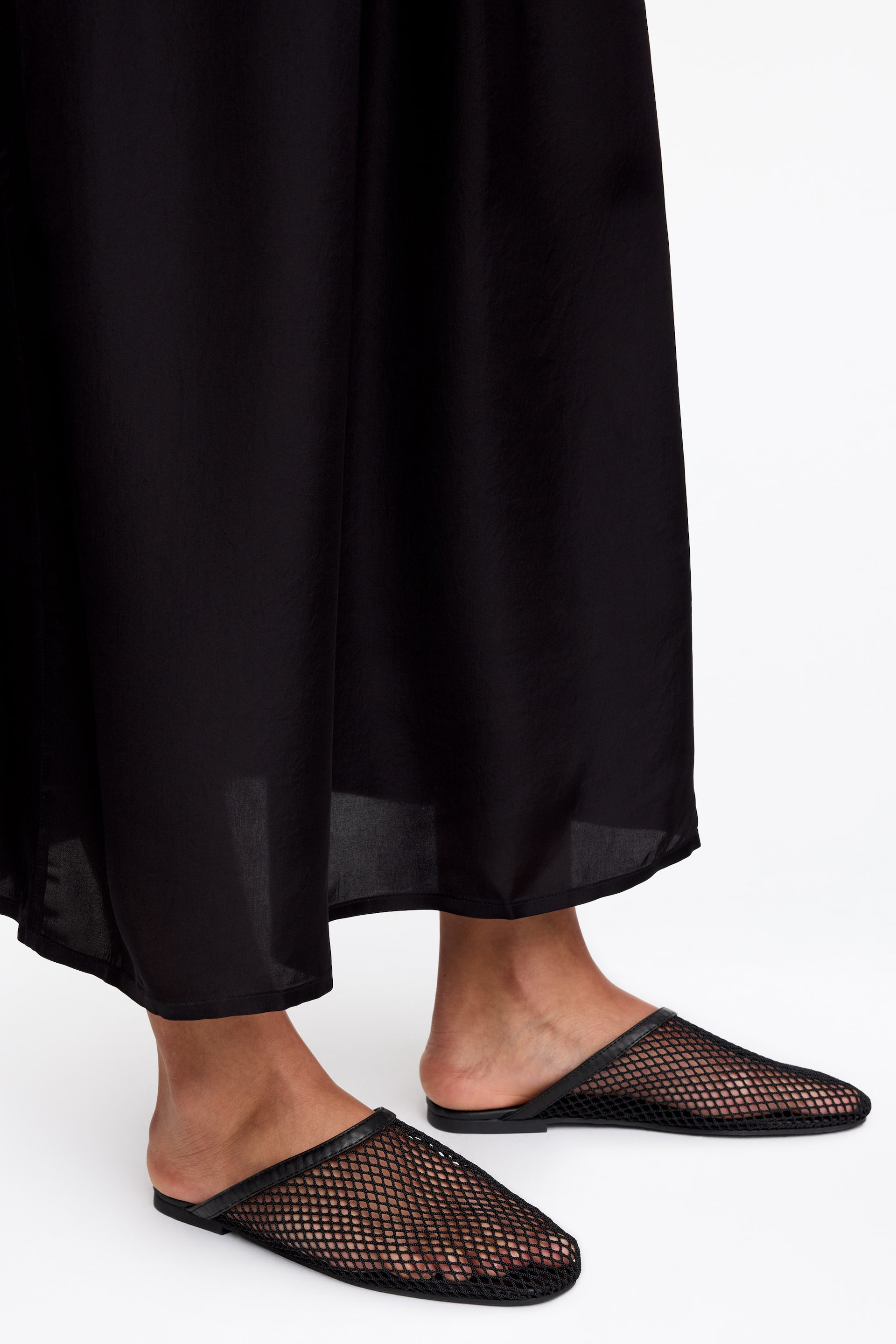 Se større billede: Sort mesh-mules har en spids tå, en sort mesh-overdel og en glat læderkant omkring åbningen og sålen. De vises på fødderne, let vinklet til siden, hvilket afslører deres åbne hældesign.