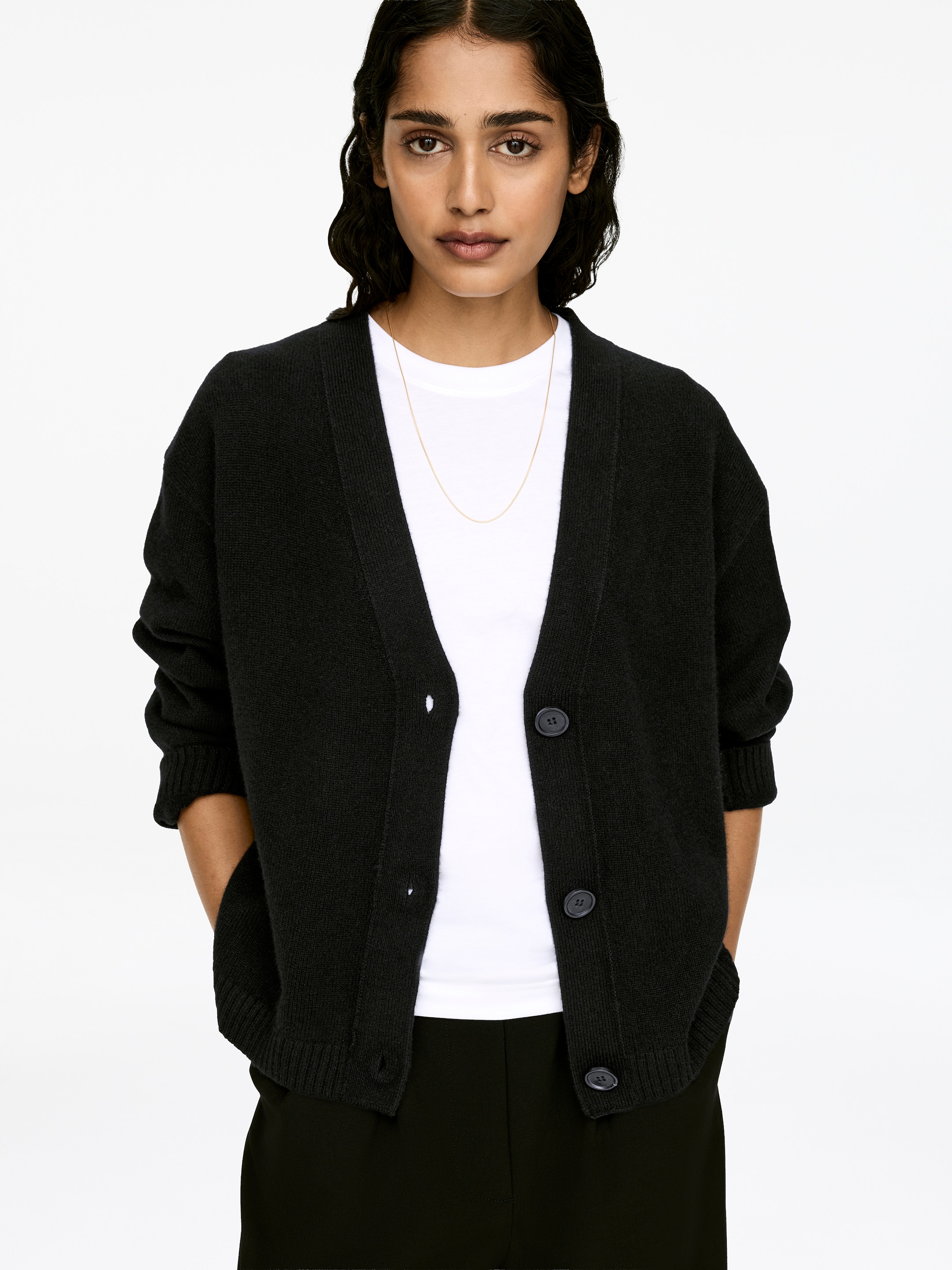 View larger image: A black long-sleeved cardigan, crafted from cashmere and wool, is being worn by the model over a white t-shirt. The cardigan features a V-neck, a button closure with several buttons remaining unfastened, and rib-knitted trims on the cuffs and hem.
