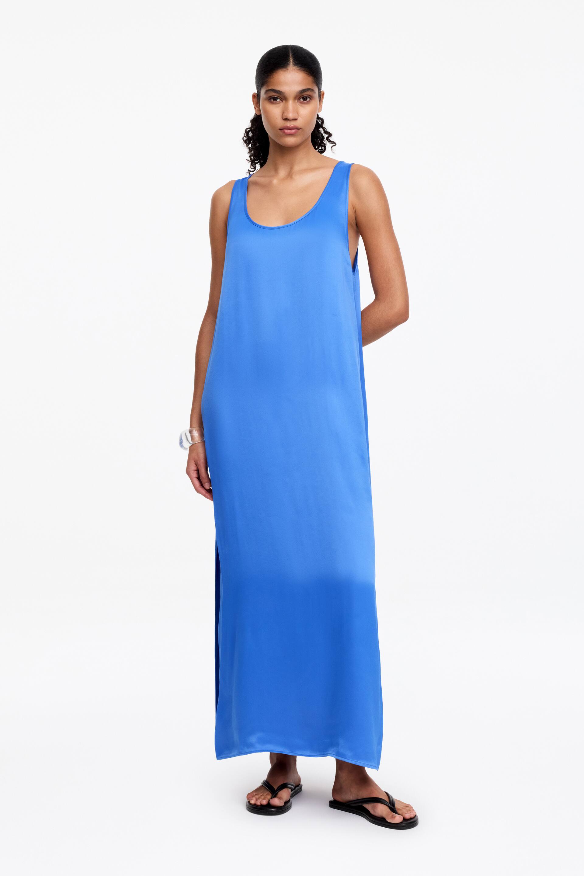 Visualizza immagine più grande: Un abito maxi blu è rivolto frontalmente, caratterizzato da uno scollo rotondo e un design senza maniche. Presenta una silhouette dritta e ampia in un tessuto liscio e fluente, con uno spacco laterale.