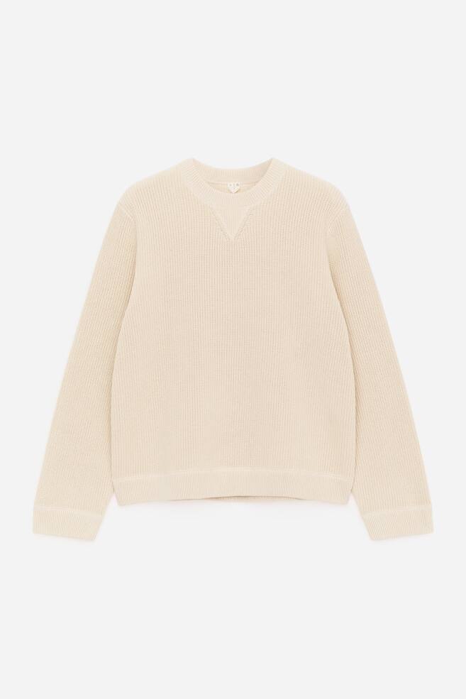 Un jersey de color crema claro se presenta de FRENTE, con un tejido de punto con textura de media trenza. Está diseñado con un cuello redondo que incluye un detalle de inserción en V y se completa con detalles de canalé en el cuello, los puños y el dobladillo, presentando un ajuste regular. - 1