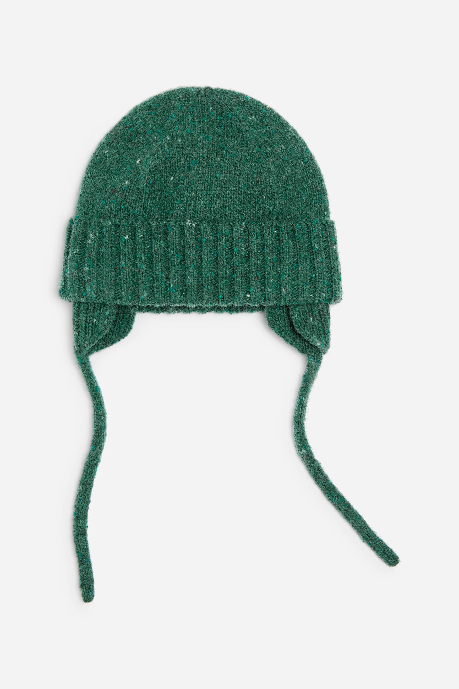 Ver imagem maior: Um gorro verde de malha com abas para as orelhas está virado para a frente, apresentando uma dobra canelada grossa e um corpo em fio texturado com pequenos salpicos multicoloridos subtis. Longos atilhos de malha a condizer pendem de cada aba.
