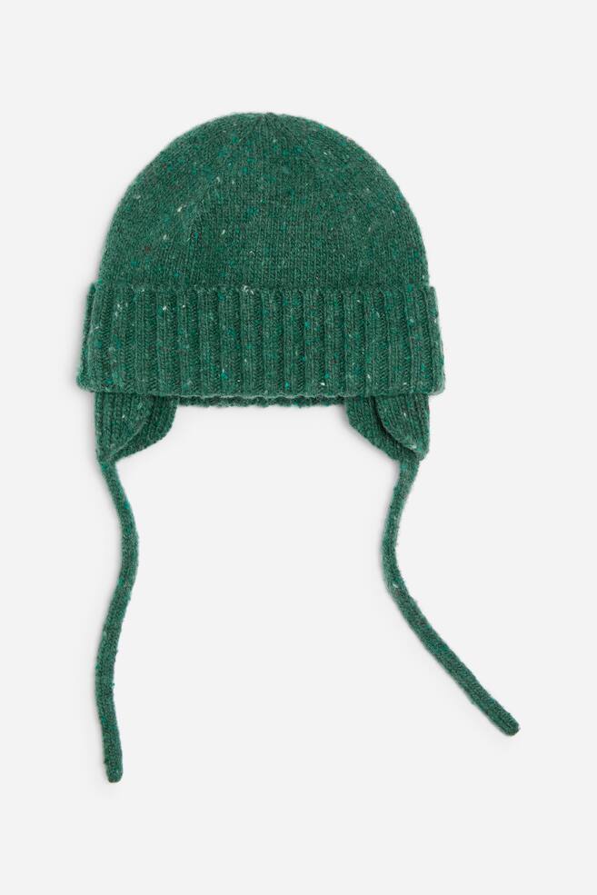 Eine grÃ¼ne gestrickte OhrenschÃ¼tzer-MÃ¼tze ist von vorn zu sehen und verfÃ¼gt Ã¼ber einen dicken gerippten Umschlag sowie einen strukturierten, melierten GarnkÃ¶rper mit dezenten mehrfarbigen Sprenkeln. Lange, passende StrickbÃ¤nder hÃ¤ngen von jedem Ohrenschutz herab. - 1