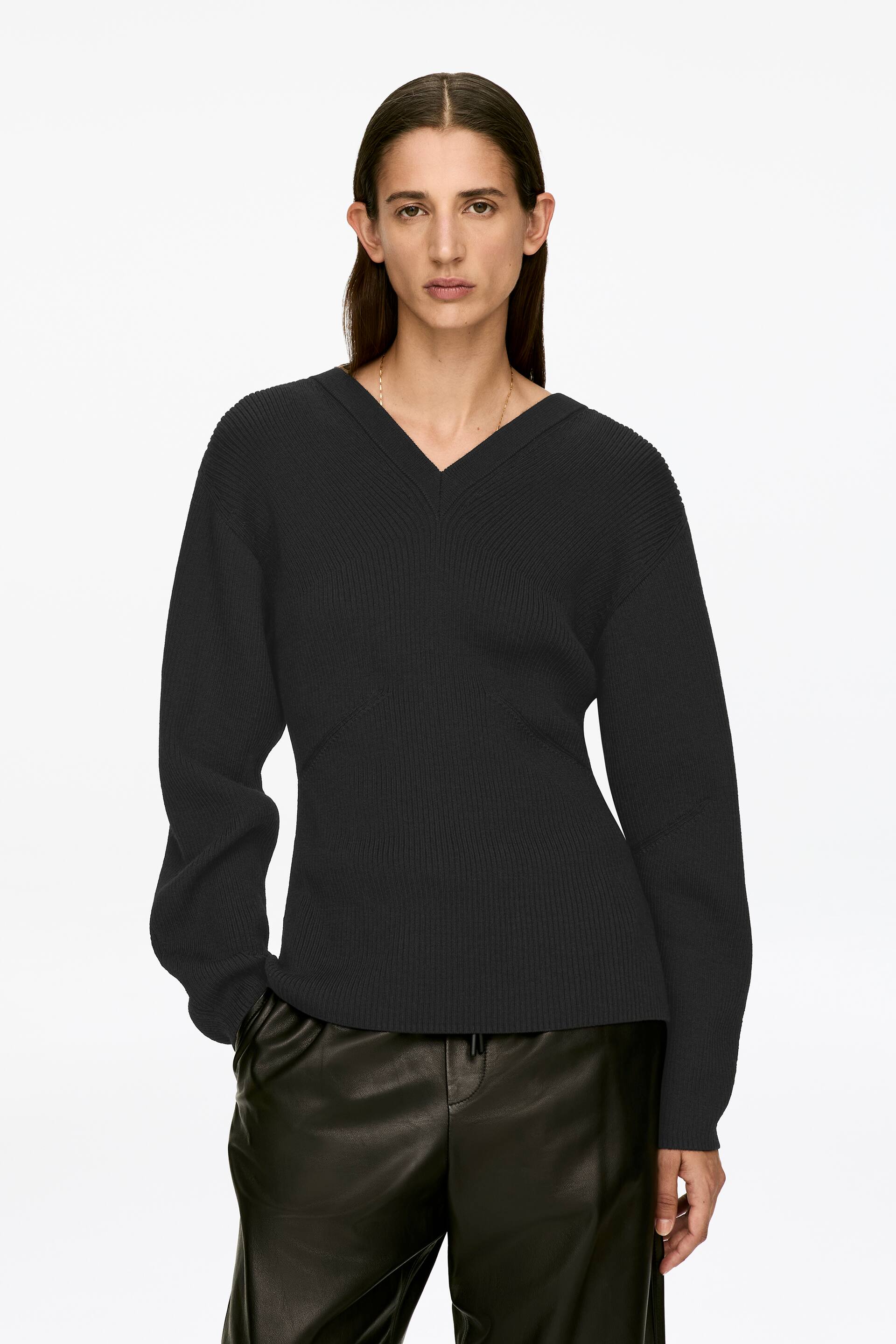 Vis større bilde: En svart ribbestrikket genser med V-hals og vanlig passform bæres av modellen. Modellen står med en hånd hvilende i en bukselomme, noe som subtilt påvirker genserens fall.