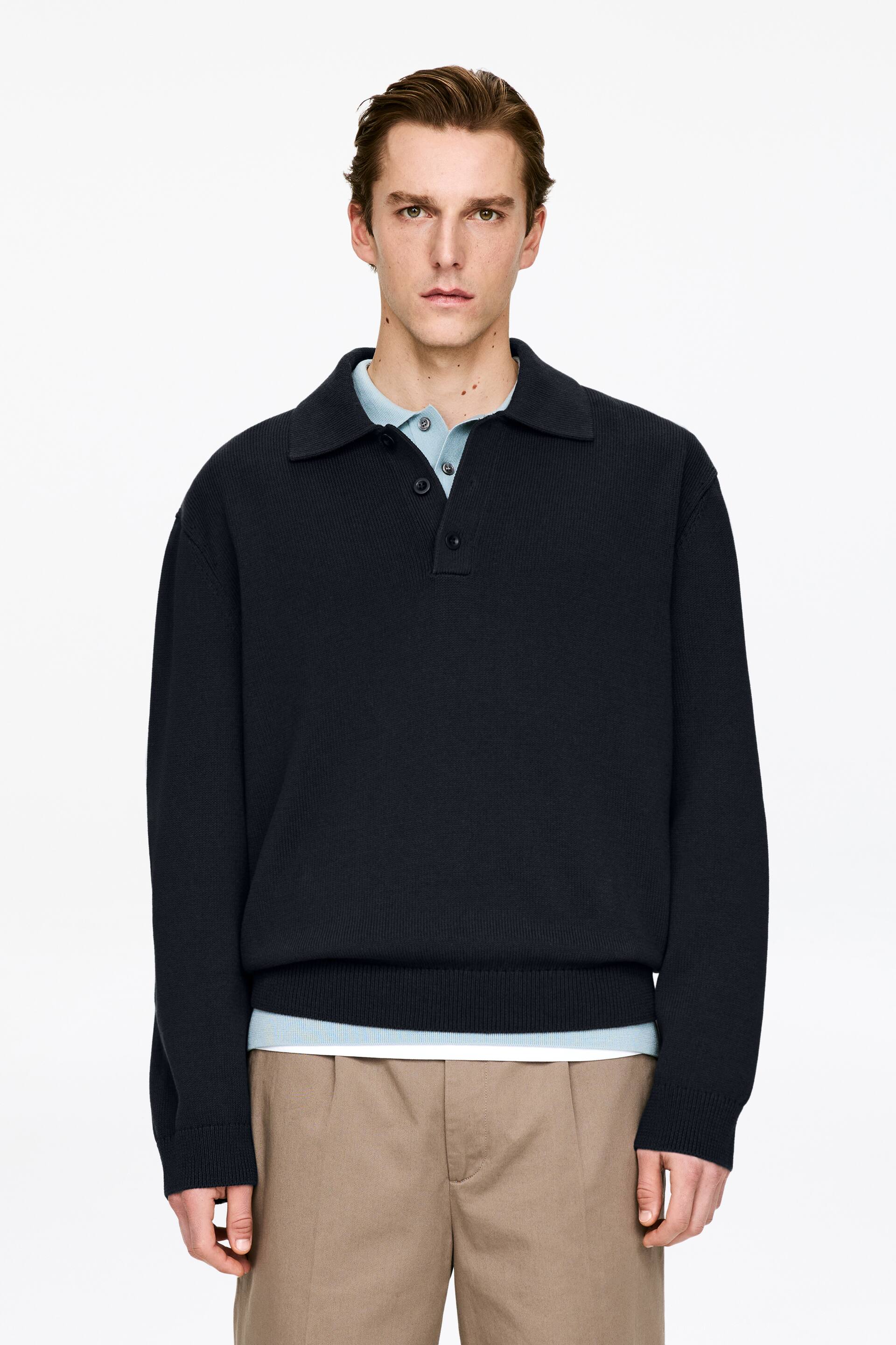 View larger image: A dark blue ribbed knit polo jumper is facing forward, featuring a polo collar, a two-button placket, long sleeves with ribbed cuffs, and a ribbed hem. A light blue polo shirt is visible layered underneath the jumper.